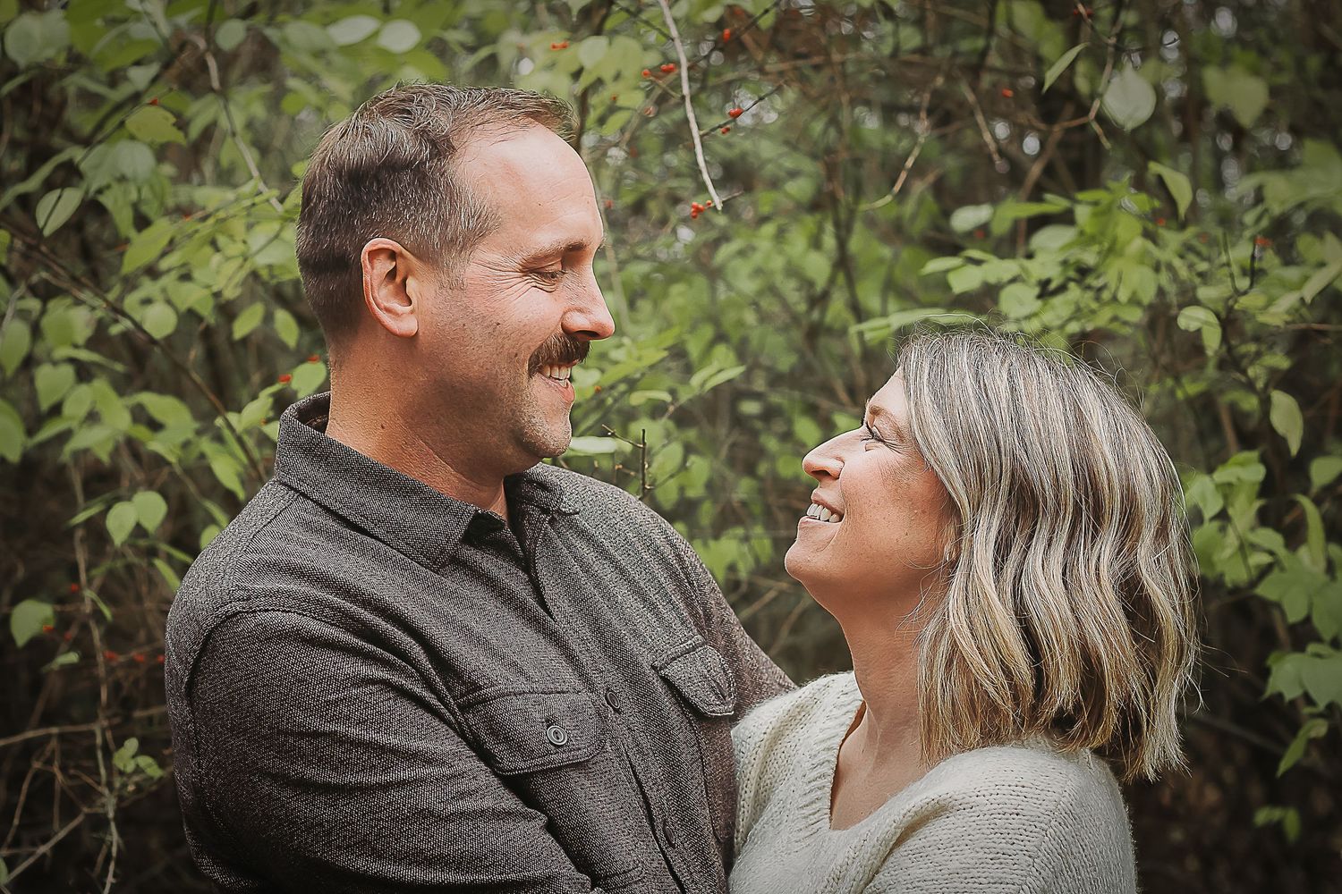 A couple in autumn clothing share affectionate moments while walking together through a lush garden setting.