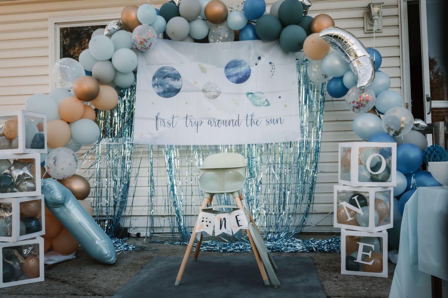 Baby shower party decorations featuring blue and beige balloon garlands with cloud themed backdrop and table settings.