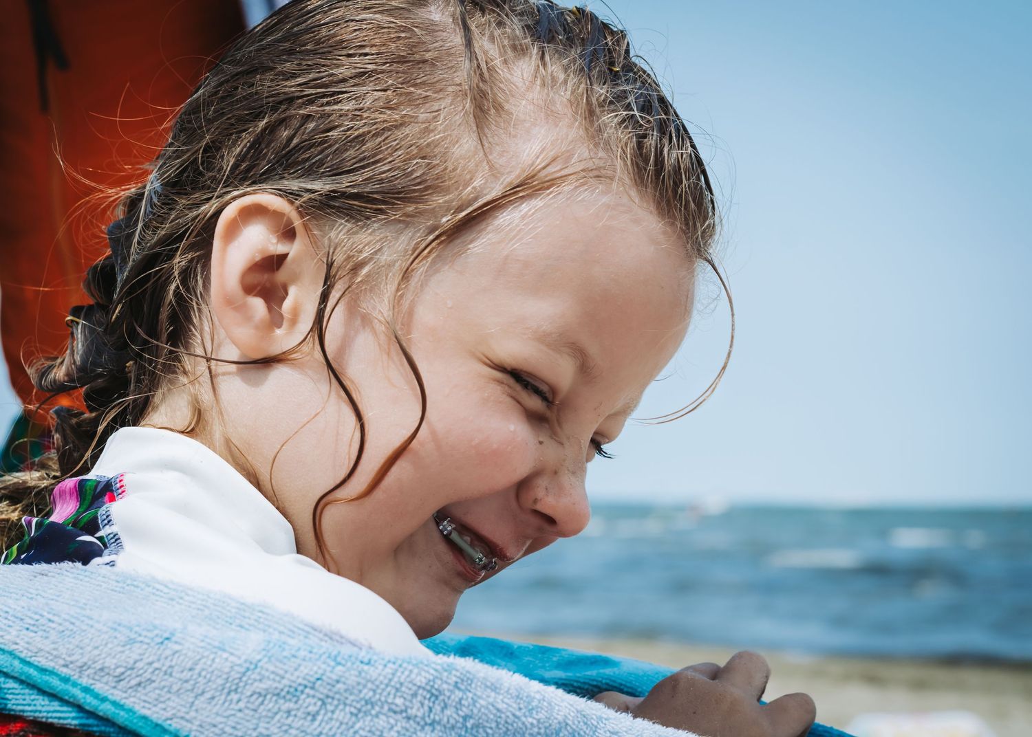Child in sunhat enjoying sunny day at beach with bright blue ocean and sky in background.