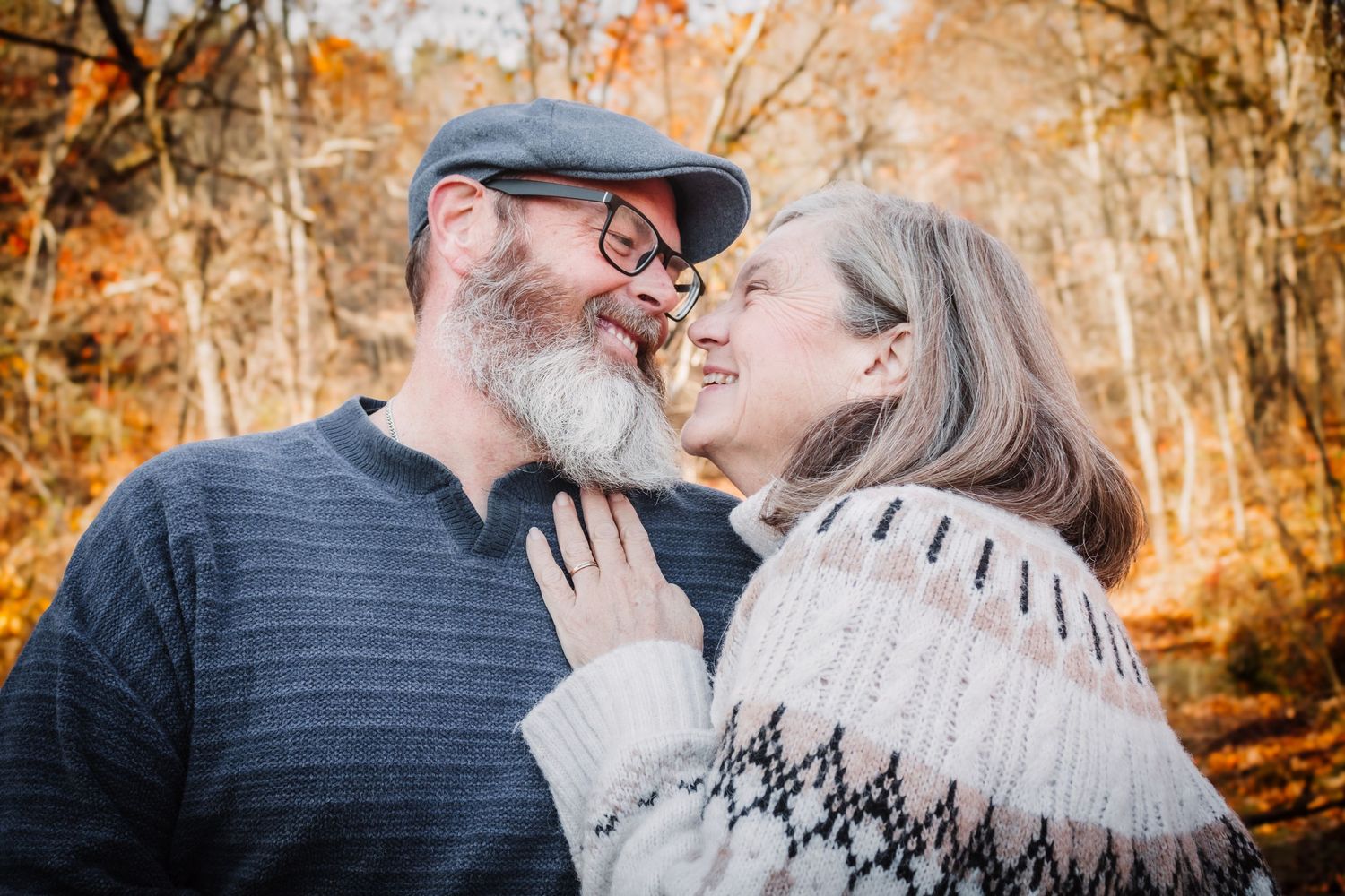 Two people share an intimate moment in golden autumn woods while wearing casual clothing and embracing.