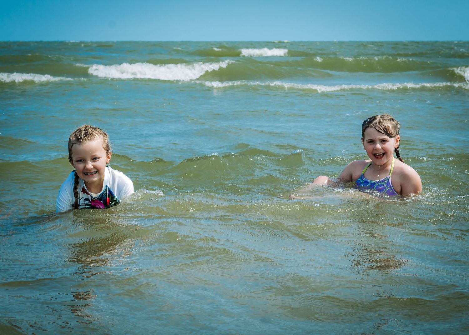 Small waves break along a beach shoreline during a sunny summer day at the water's edge.