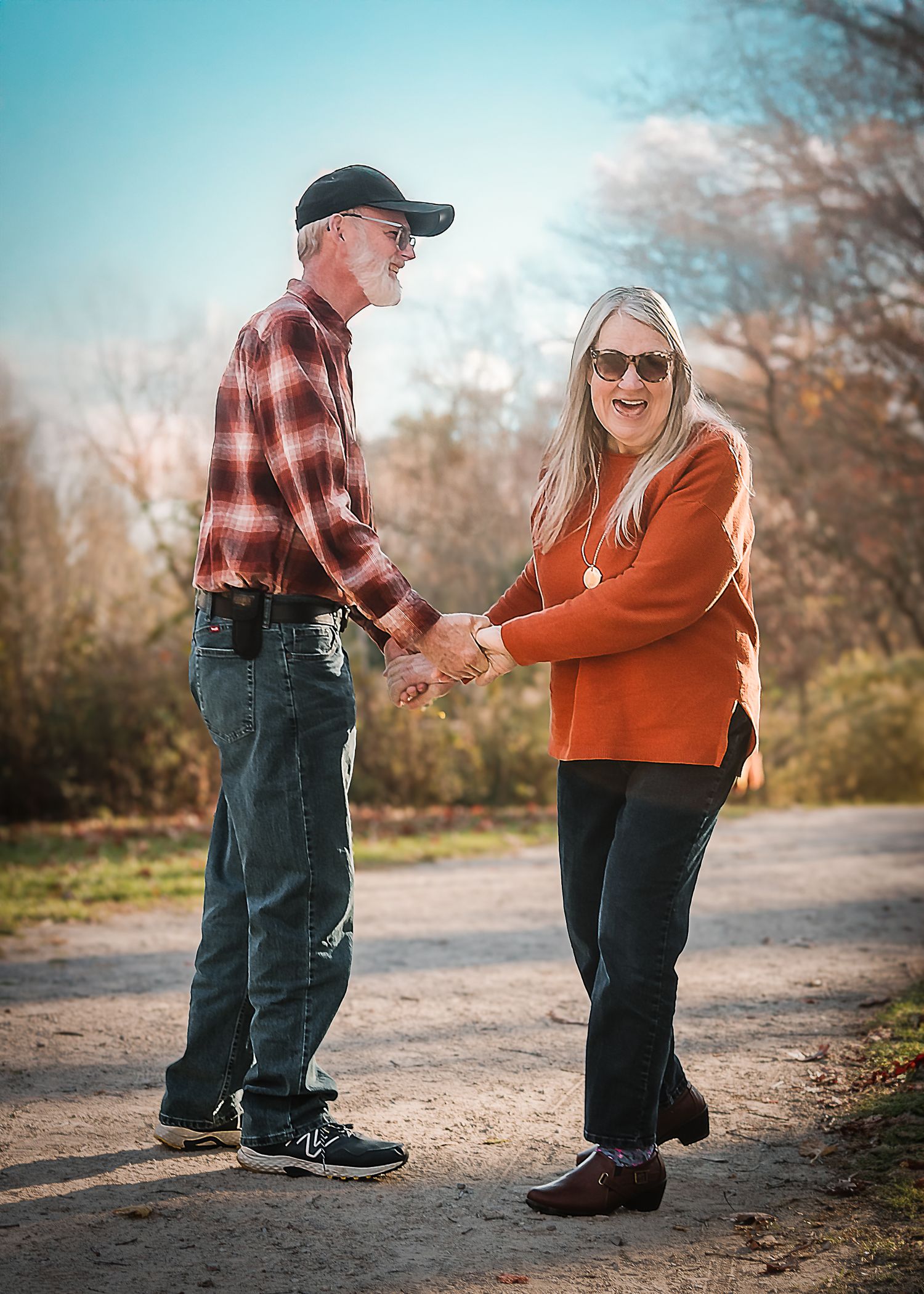 A couple in casual attire walks along an autumn path holding hands in a romantic outdoor setting.