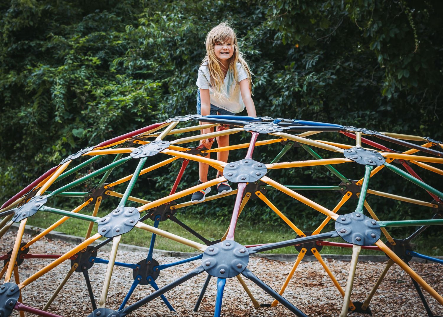 Children climbing on colorful geometric playground equipment in park setting.