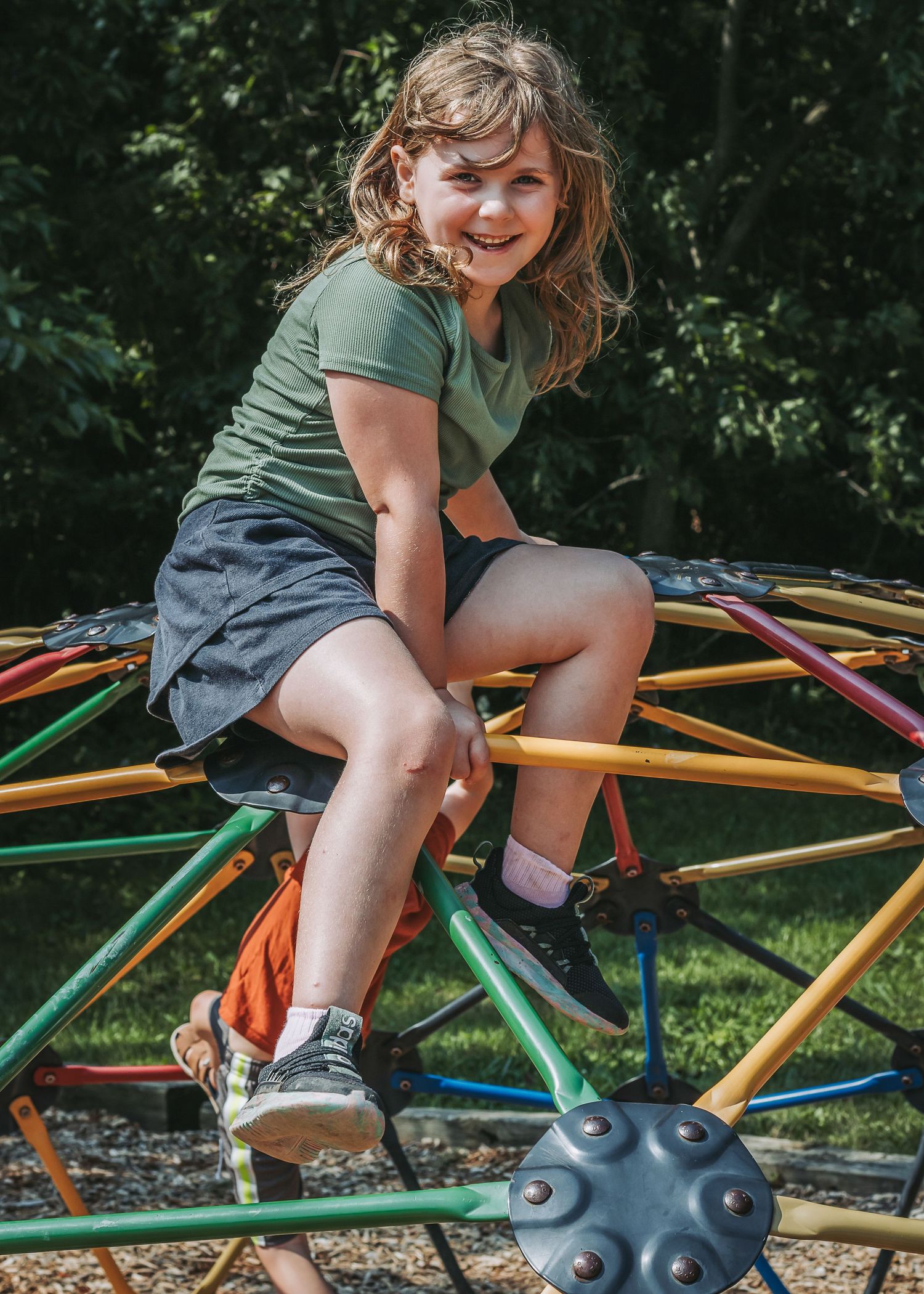 Child playing on colorful geometric climbing dome structure at outdoor playground in sunny weather.