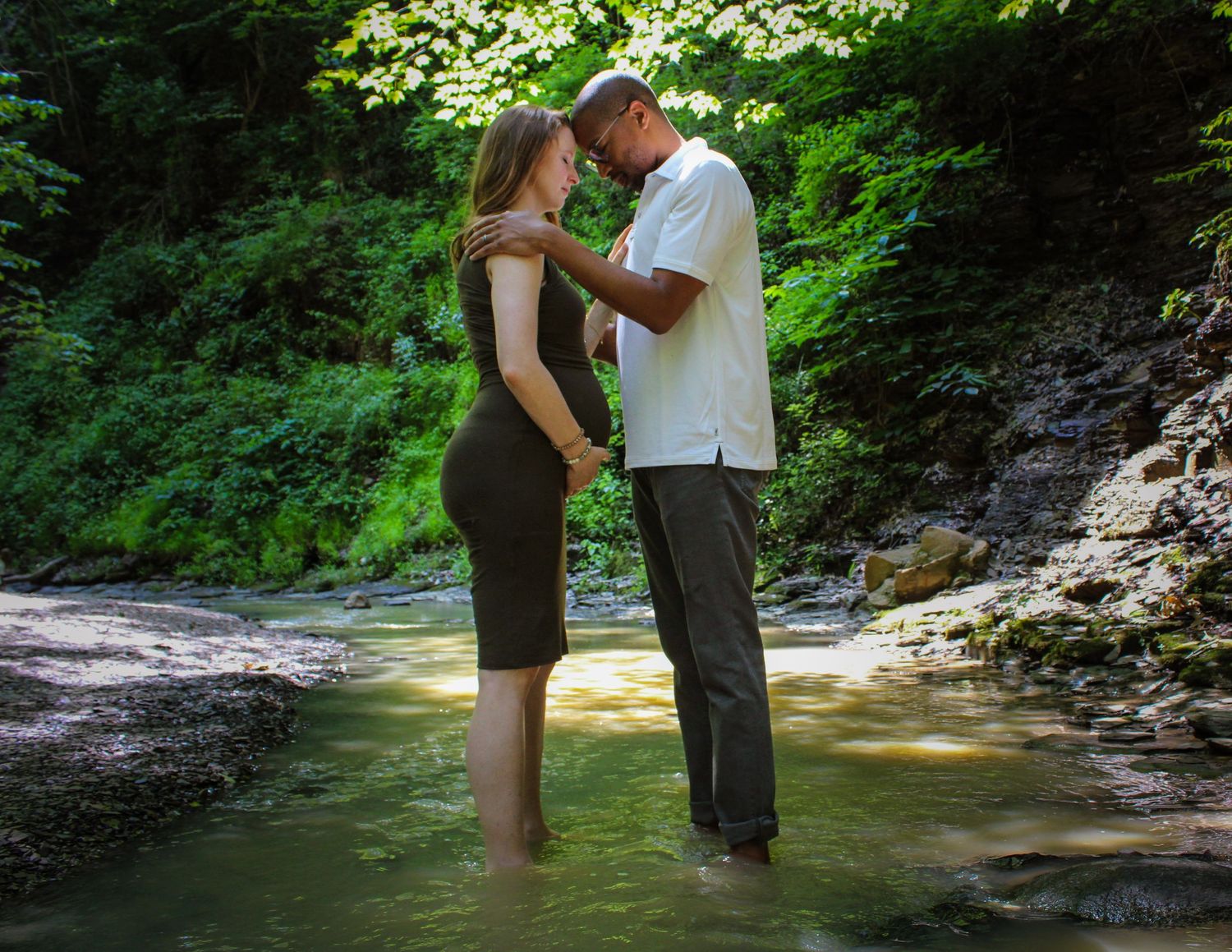 A couple embraces near a scenic waterfall in a lush forest setting during an engagement photo session.
