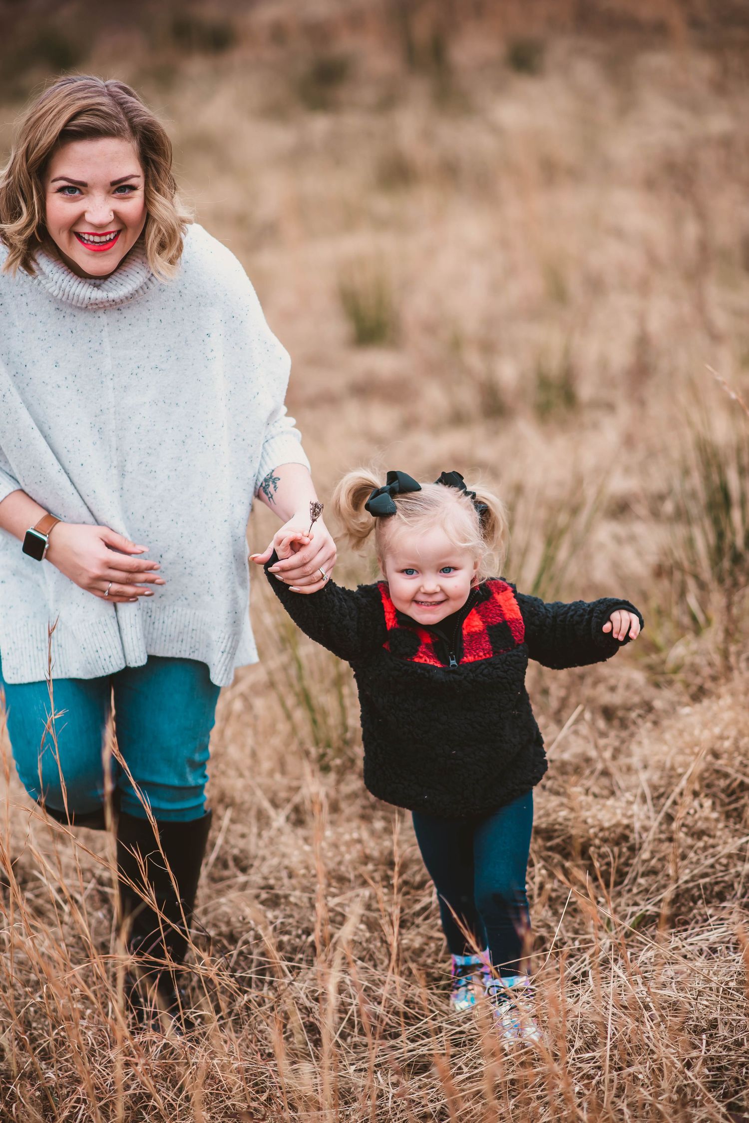 A playful moment captured in a dry grassy field showing jeans and light colored sweaters in motion.