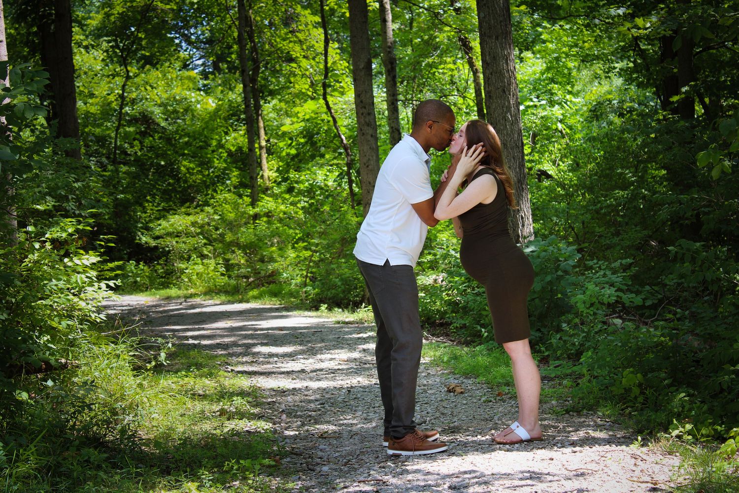 A scenic wooded hiking path with sunlight filtering through lush green trees shows people sharing a peaceful walk.