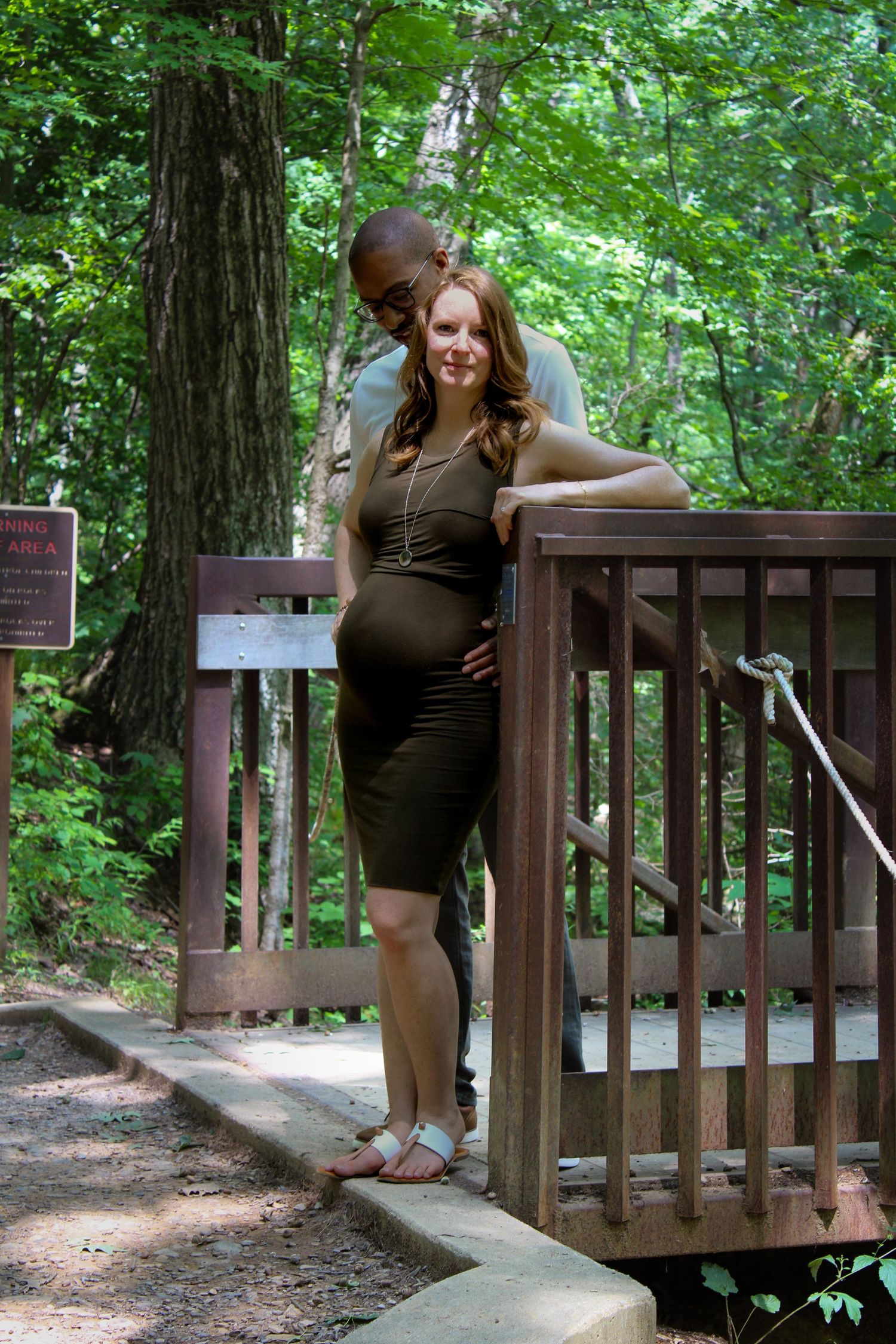 A dark-clothed figure poses in four sequential photos on a wooden deck railing surrounded by lush green forest.