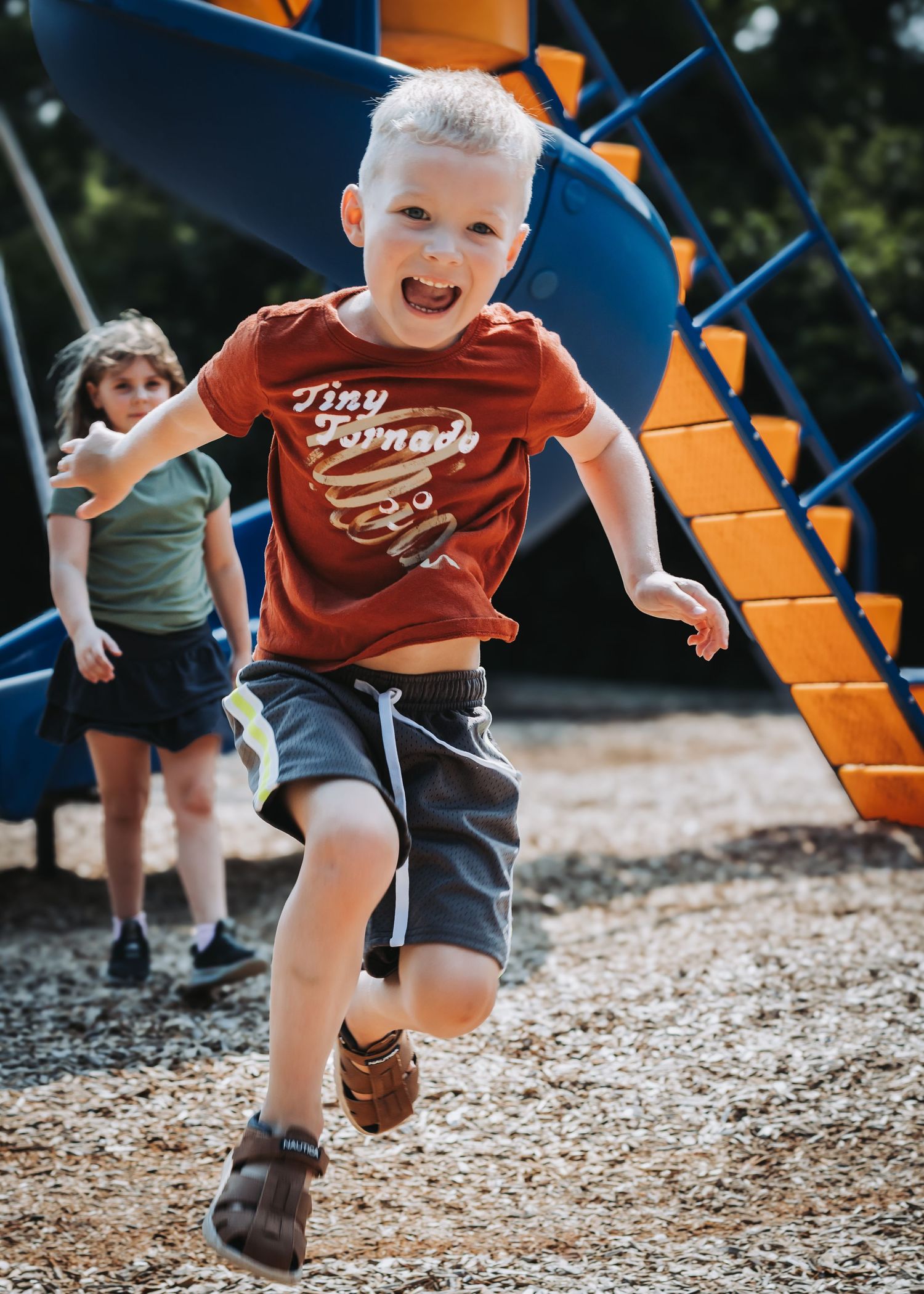 Child running and playing on playground with orange climbing structure.