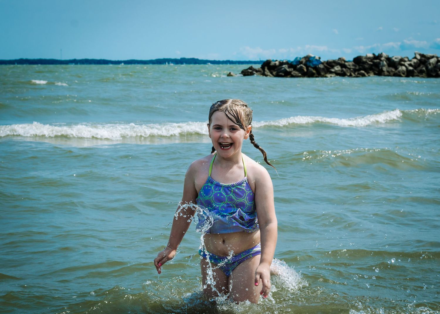 Small child splashes and plays in the gentle waves at the beach on a bright summer day.