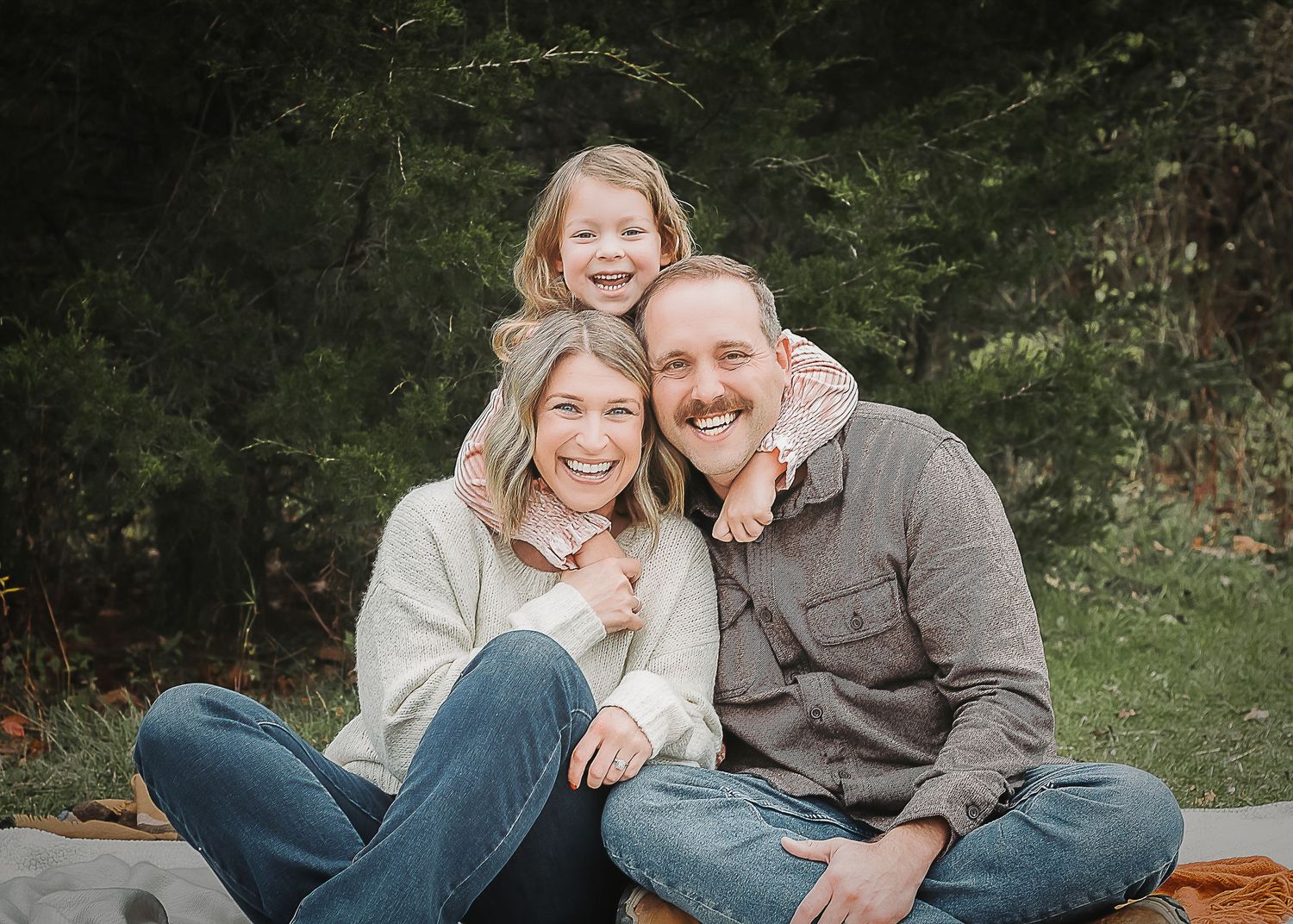 Outdoor photography session on a blanket featuring a couple sitting close together and laughing in a natural setting.