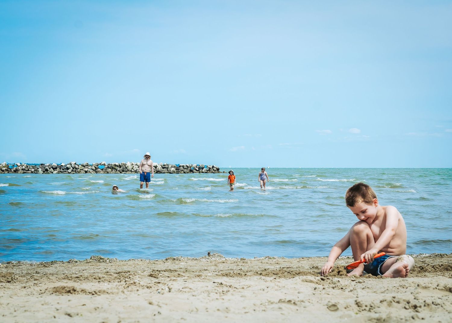 Children play together on a sunny beach near the ocean's edge while splashing in shallow water and sand.