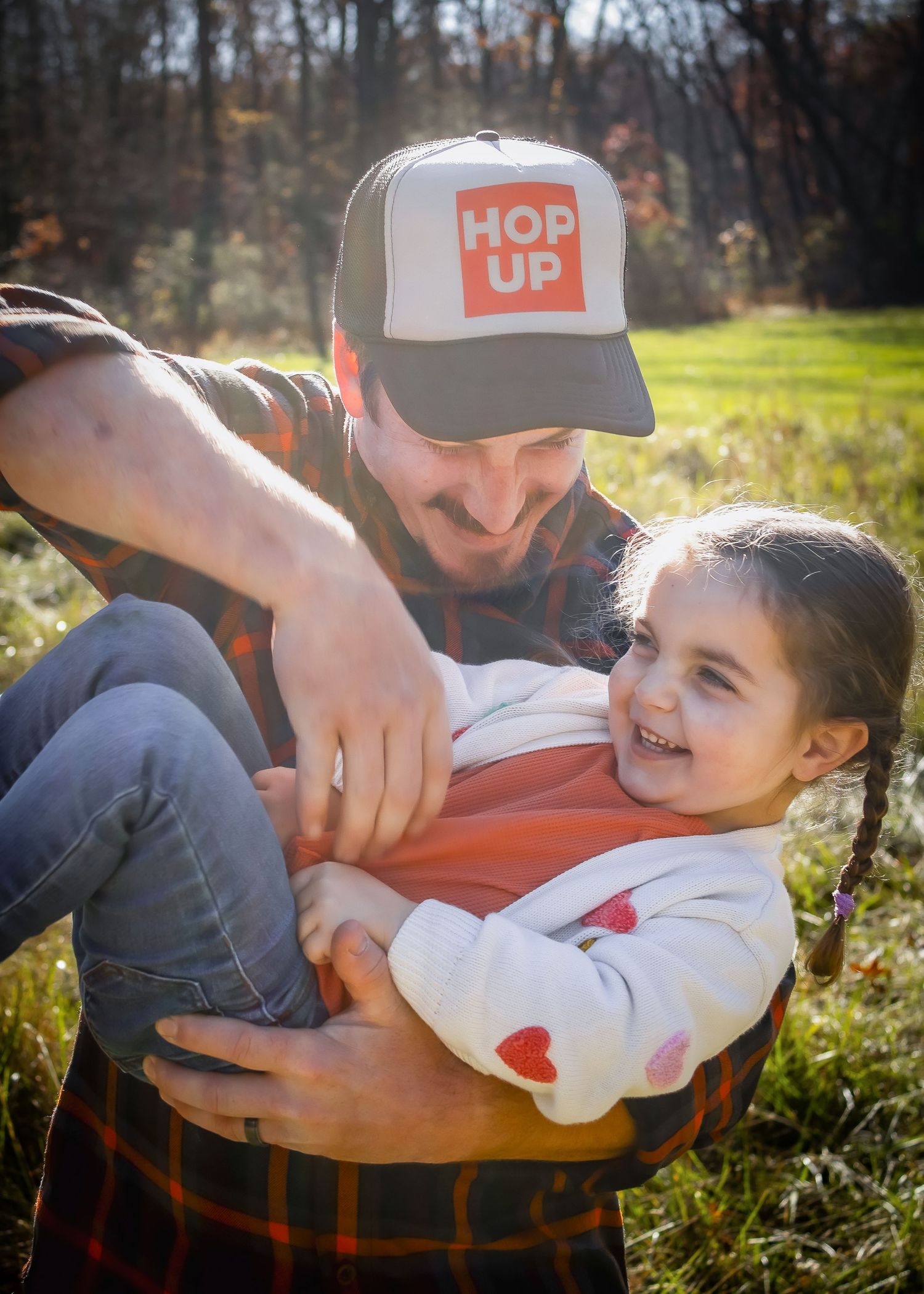 A playful tickle fight moment outdoors on a sunny autumn day with fall foliage in the background.