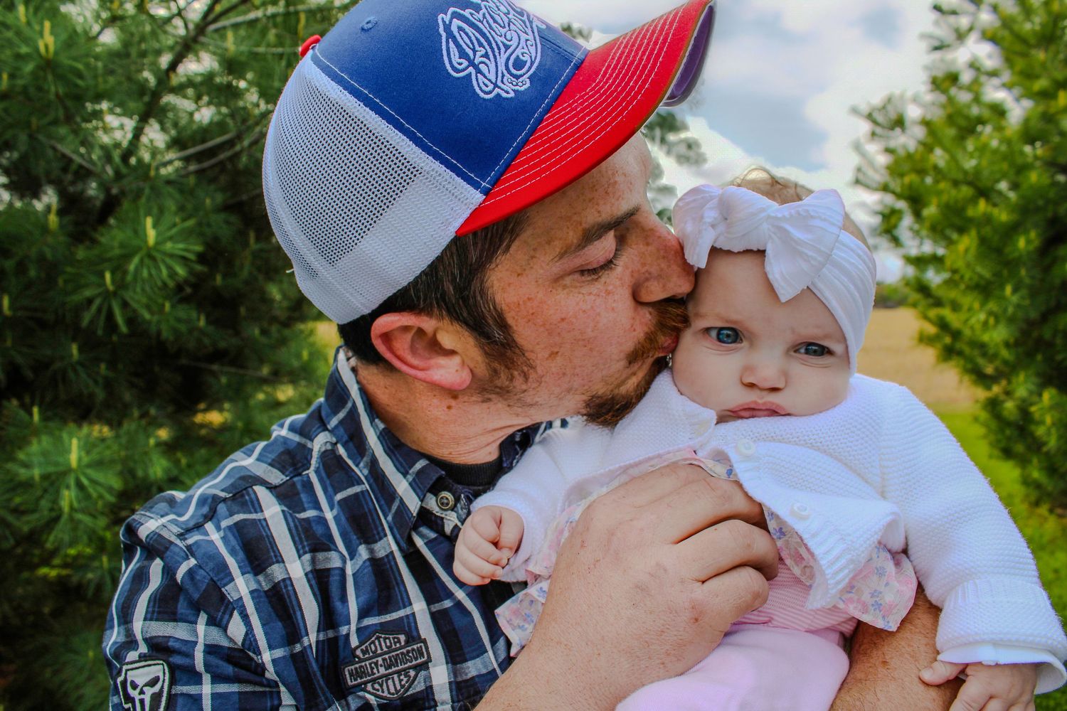 Collage shows tender moments between a parent wearing plaid and baseball cap with an infant in white clothing outdoors.