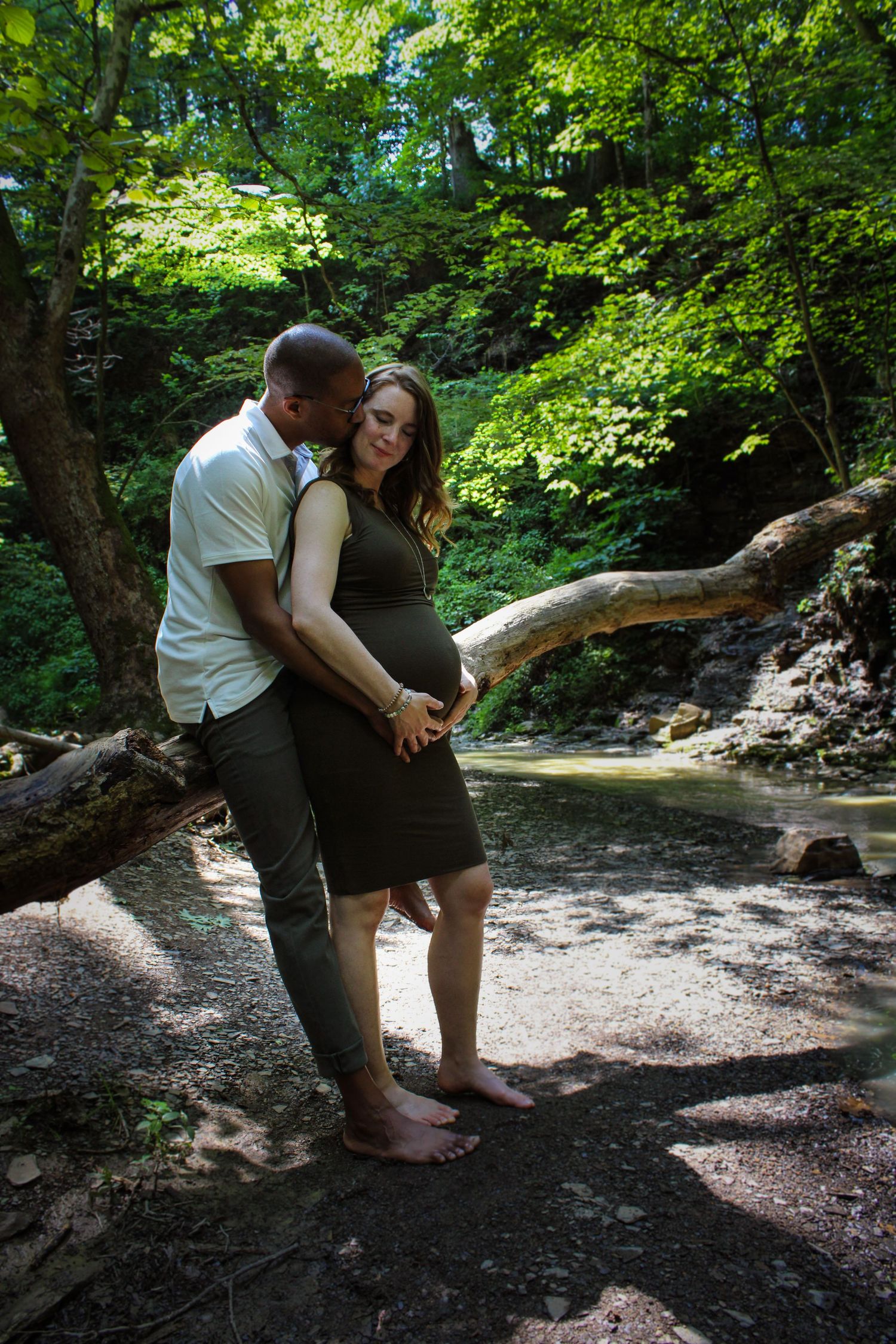 A couple walking barefoot through a lush wooded creek area on a sunny summer day.