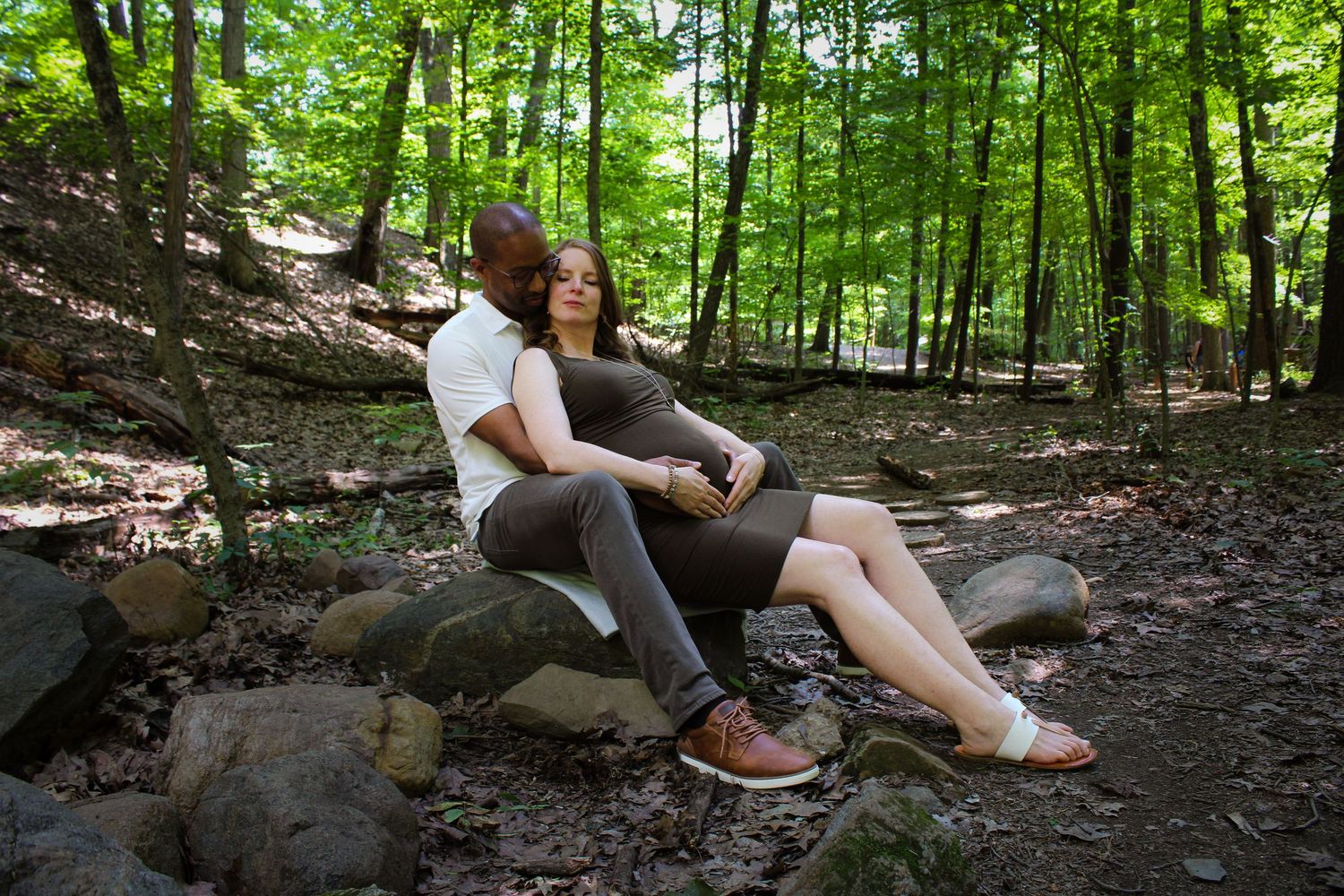 Hikers carefully navigate rocky terrain while traversing through a lush green forest path on a summer day.