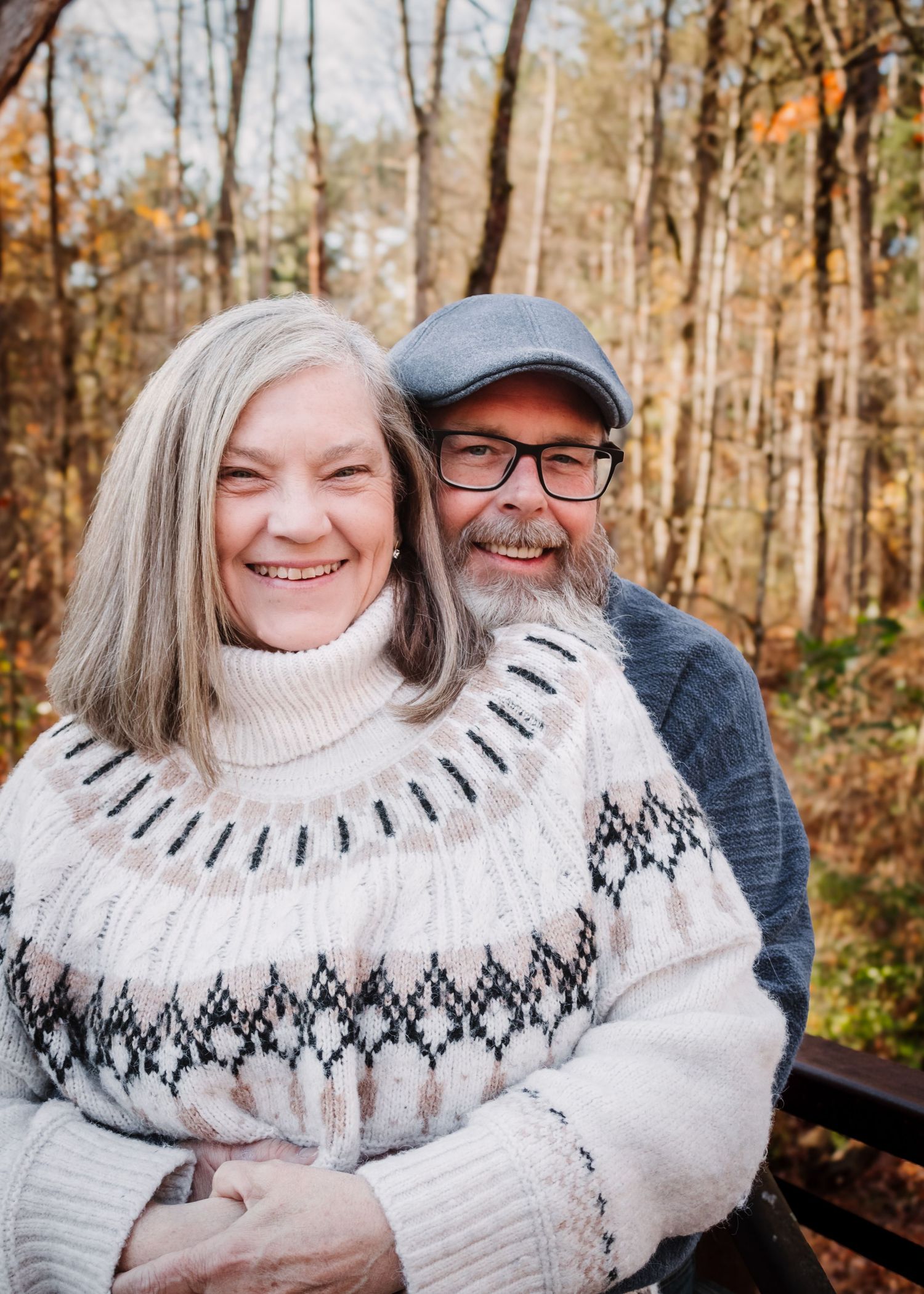 A couple enjoys a cozy autumn moment wearing matching white Nordic sweaters in a wooded setting.