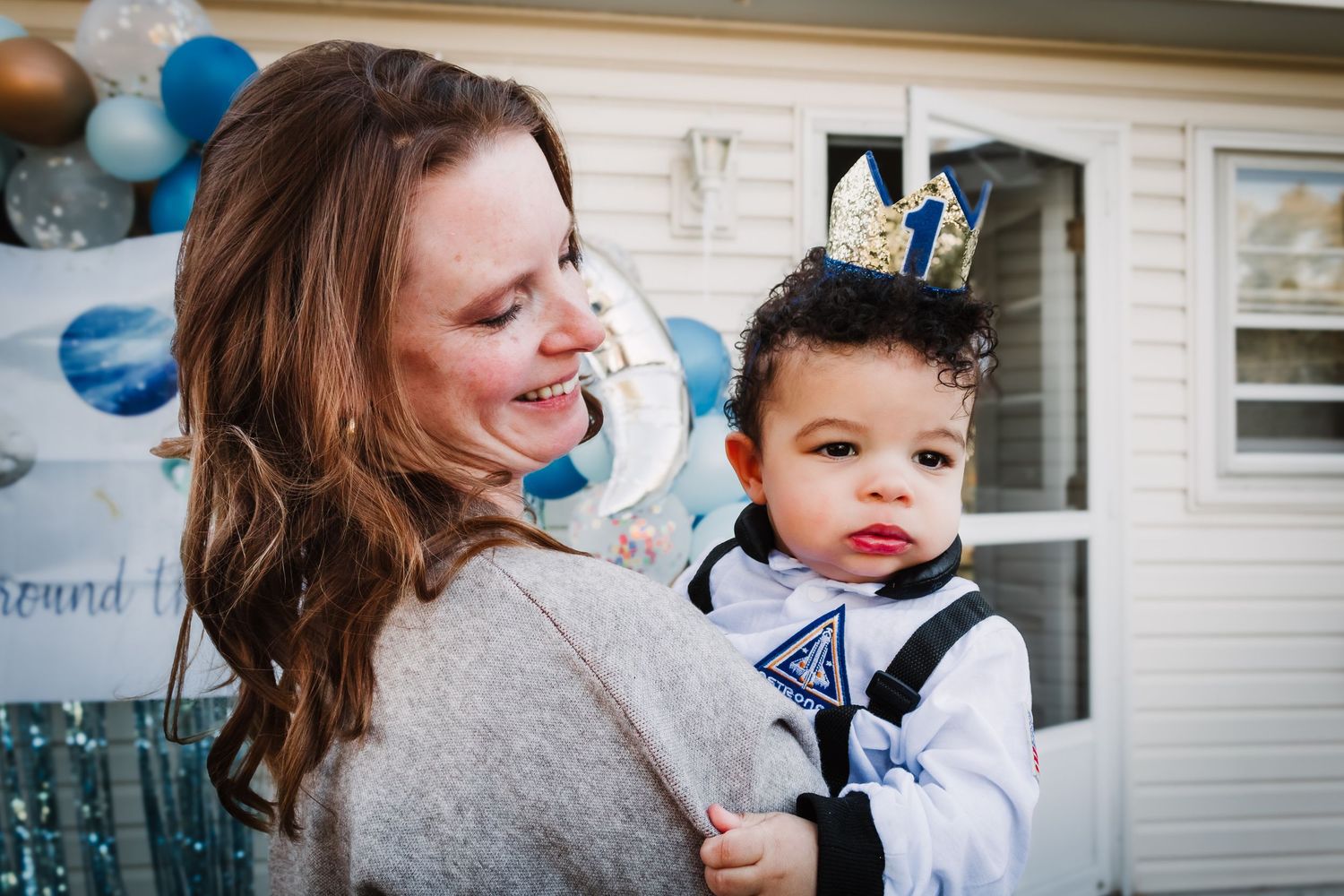 A three-panel photo collage showing a baby boy in formal wear with blue balloons at a birthday celebration.