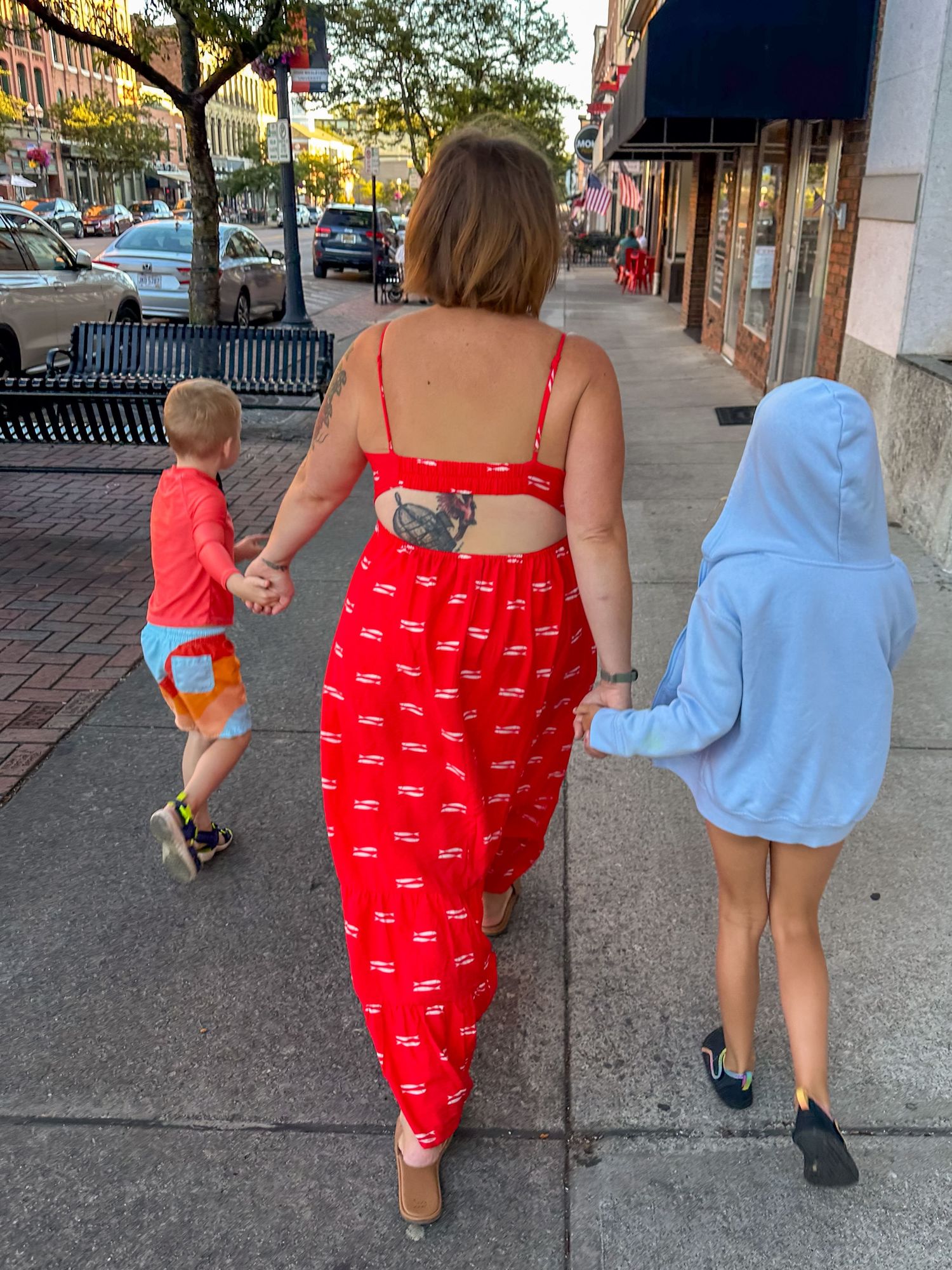 A group walking down a city sidewalk on a summer evening, with a person wearing a bright red two-piece outfit.