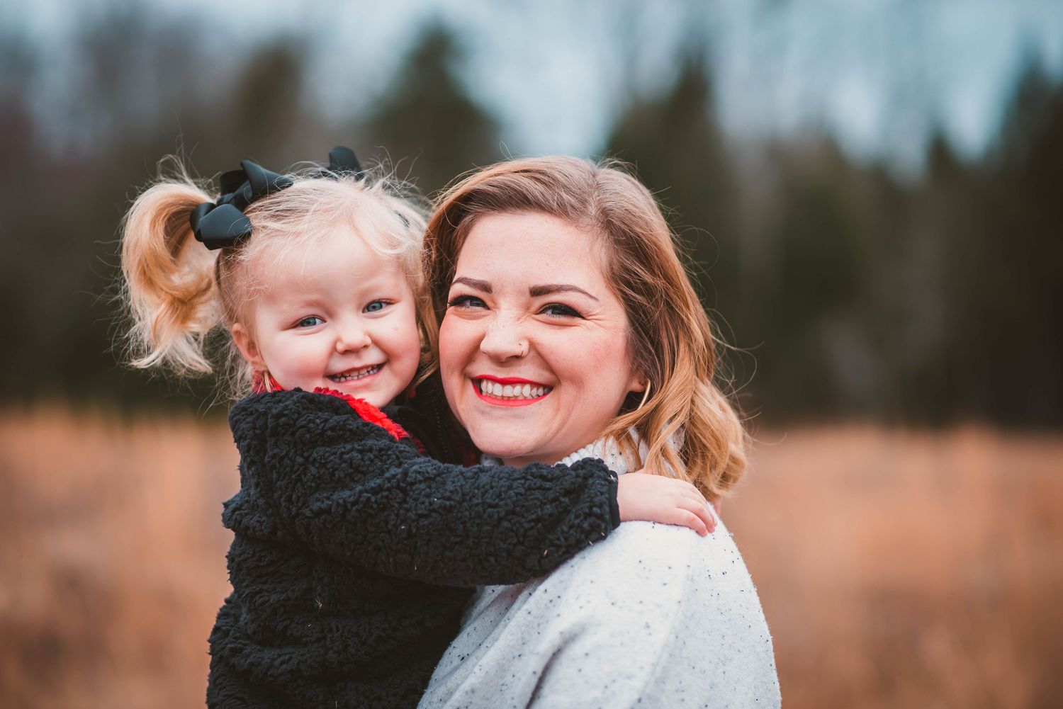 A mother and child laughing and hugging outdoors during a candid photoshoot in an autumn field at sunset.
