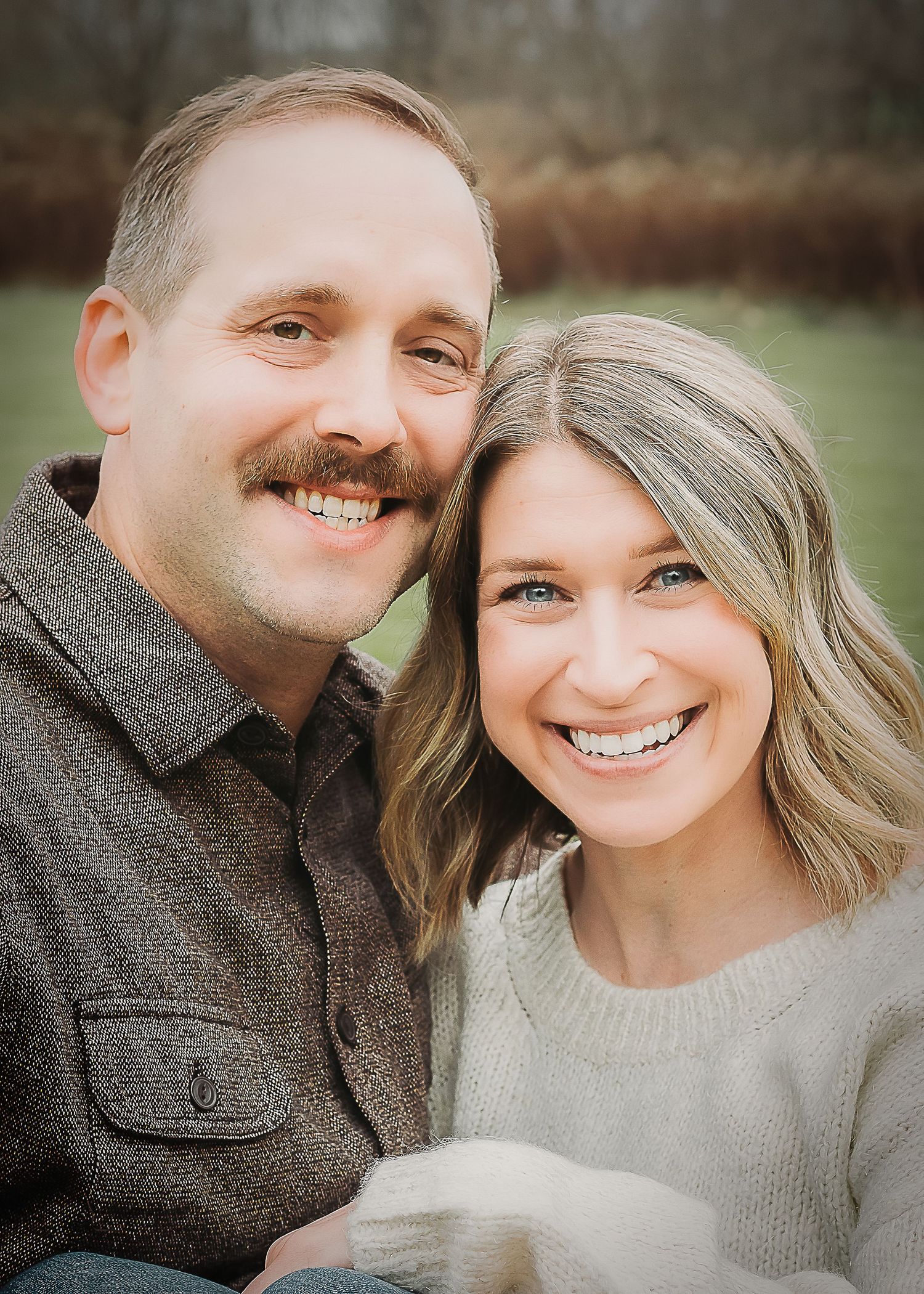 Happy couple smiles together outdoors wearing cozy sweaters on an autumn day.