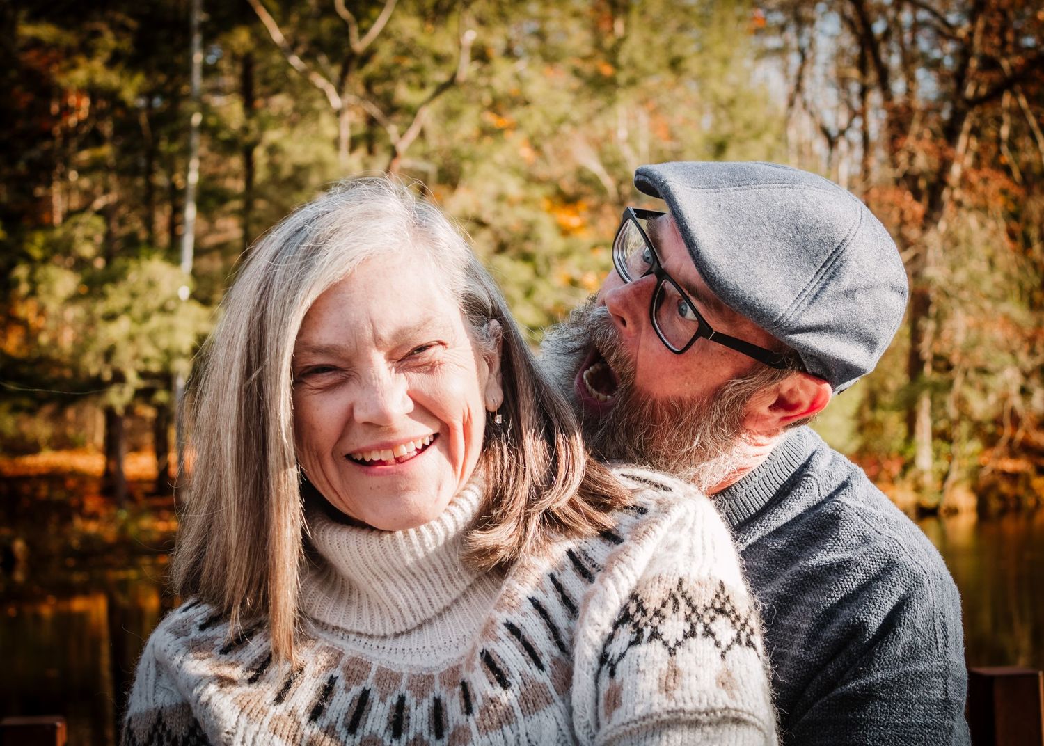 Happy couple wearing sweaters share a tender moment by an autumn lake in natural lighting.