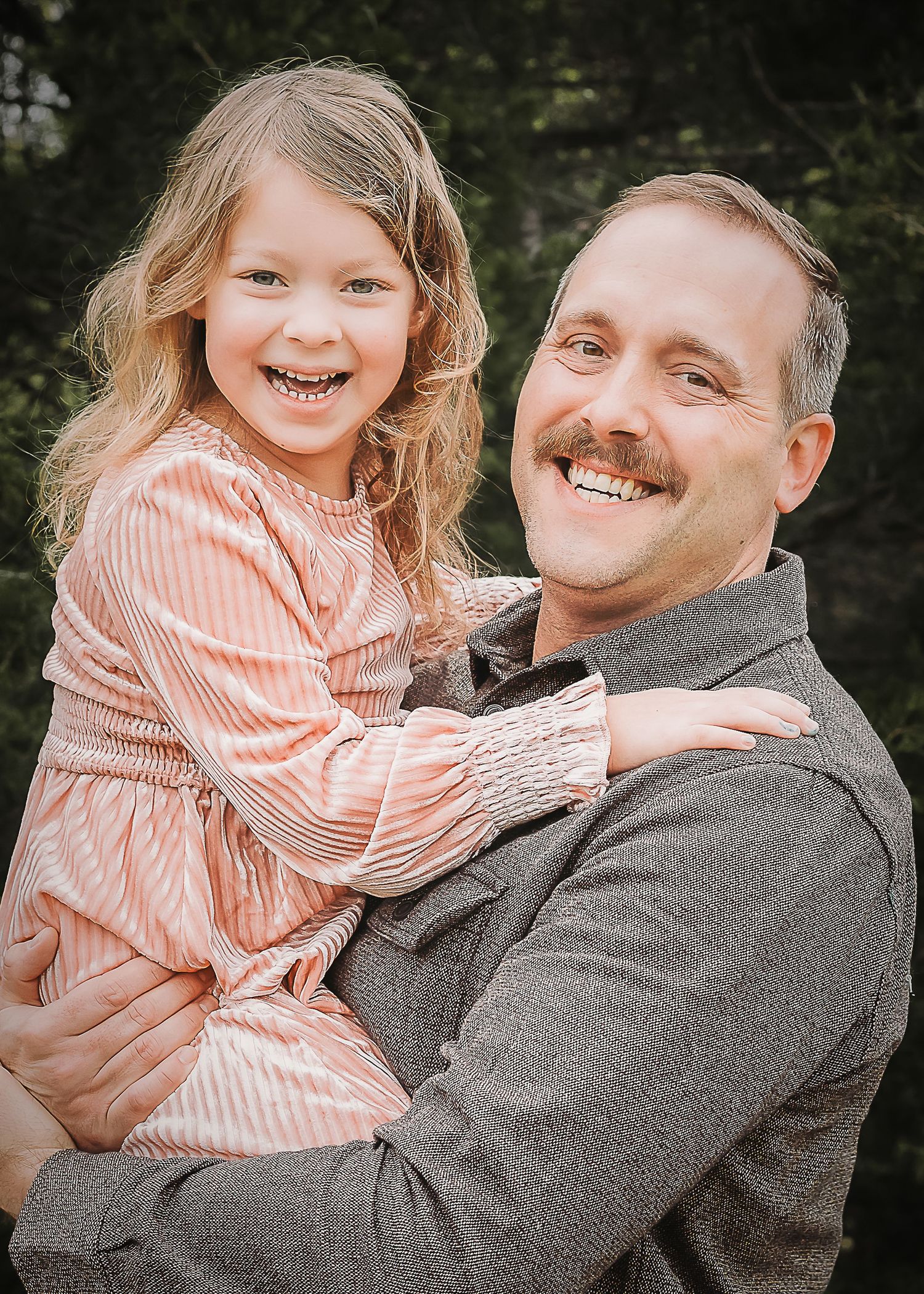 A heartwarming portrait shows a sweet moment between a child in a pink striped dress and someone in grey outdoors.