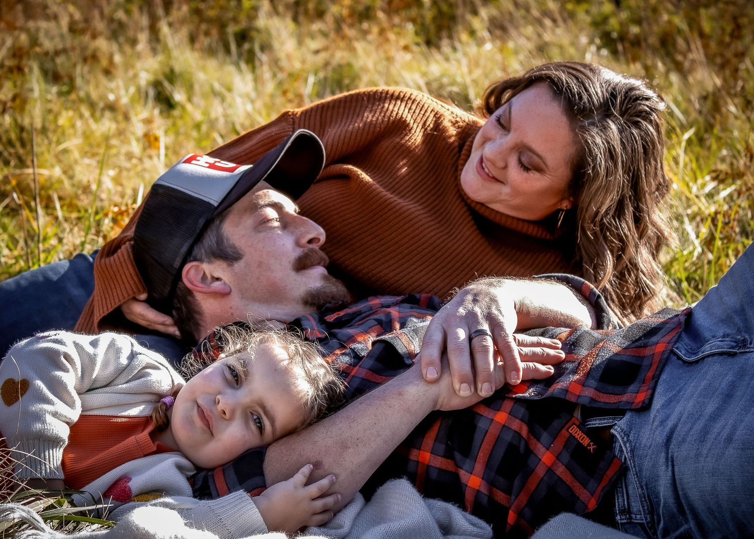 Two people lying on a plaid blanket outdoors while sharing tender moments together on a sunny autumn day.