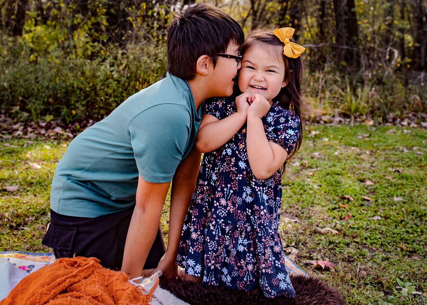 Two children playing outdoors in a grassy area surrounded by autumn trees.