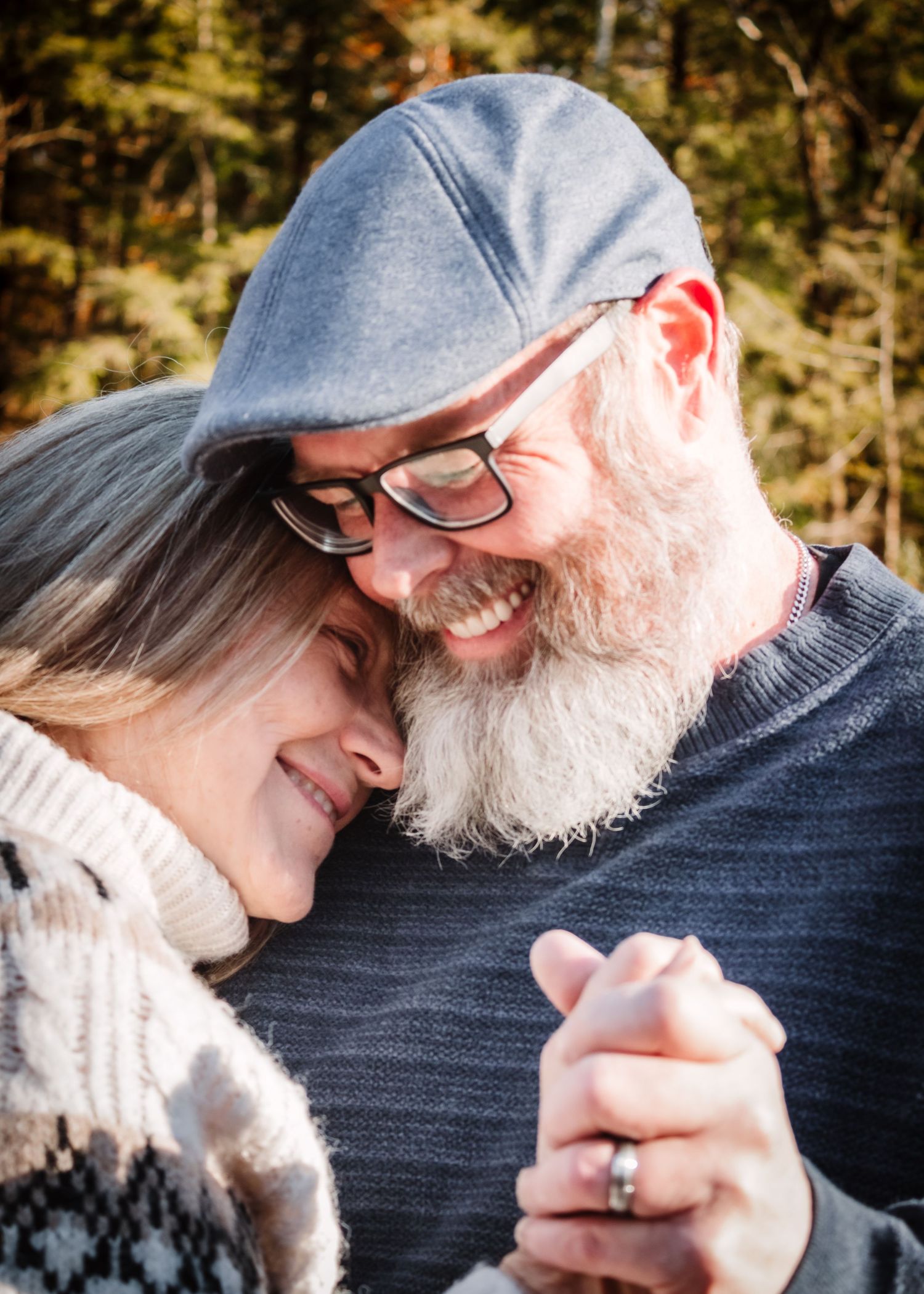 A couple shares a tender moment looking at phones together while sitting outdoors on a sunny day.