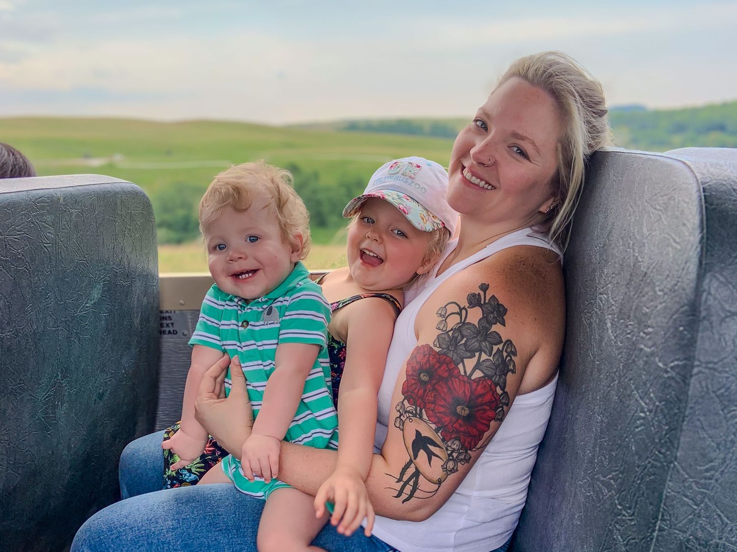 A laughter-filled moment captured on a sofa as someone holds a smiling toddler in casual summer clothes.