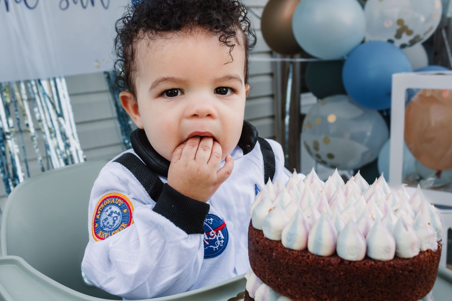 Sweet party scene with a chocolate cake decorated with pink frosting swirls and NASA-themed outfit details.