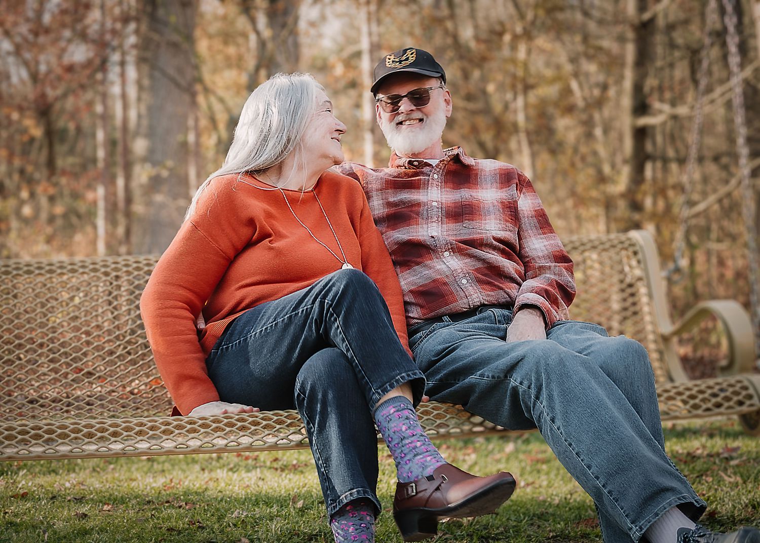 Couple in orange and plaid sit together on a hammock in an autumn forest setting.