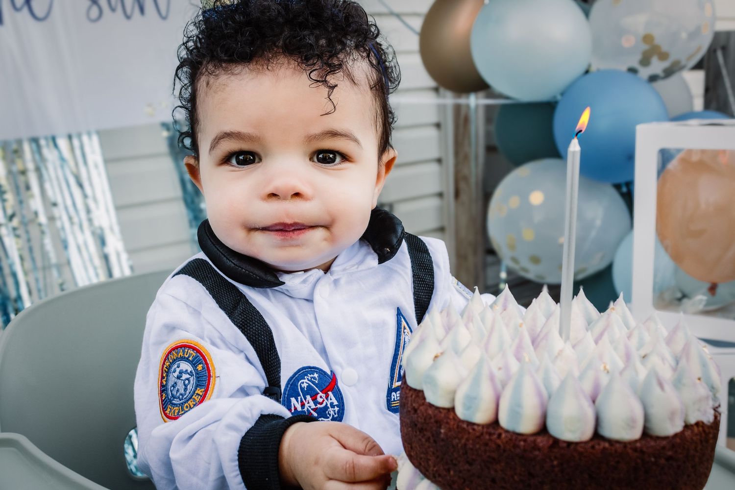 Young party guest smiles while enjoying a chocolate birthday cake surrounded by white and blue party decorations.