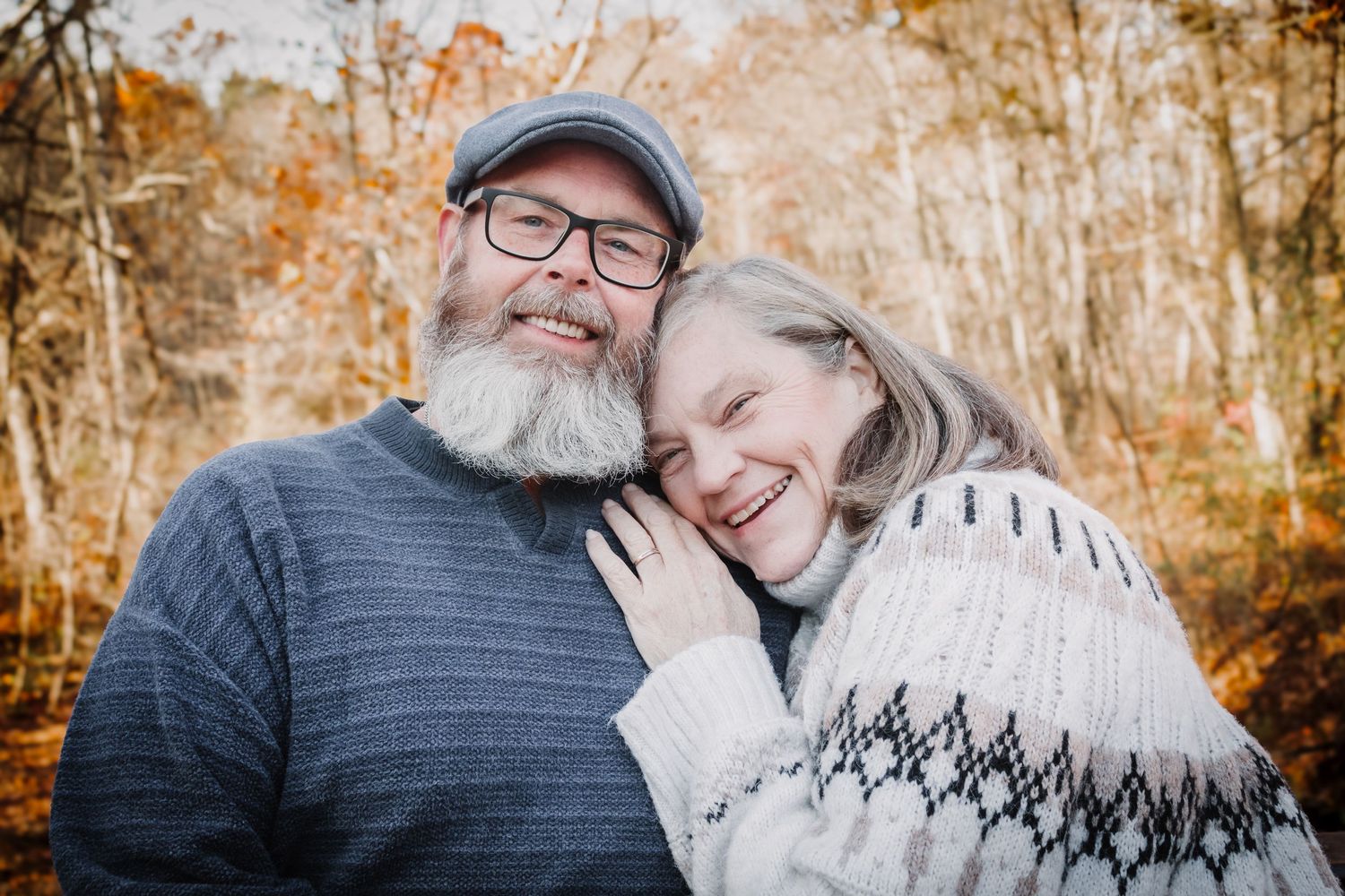 Affectionate couple enjoying autumn outdoors in a warm embrace with fall foliage in the background.