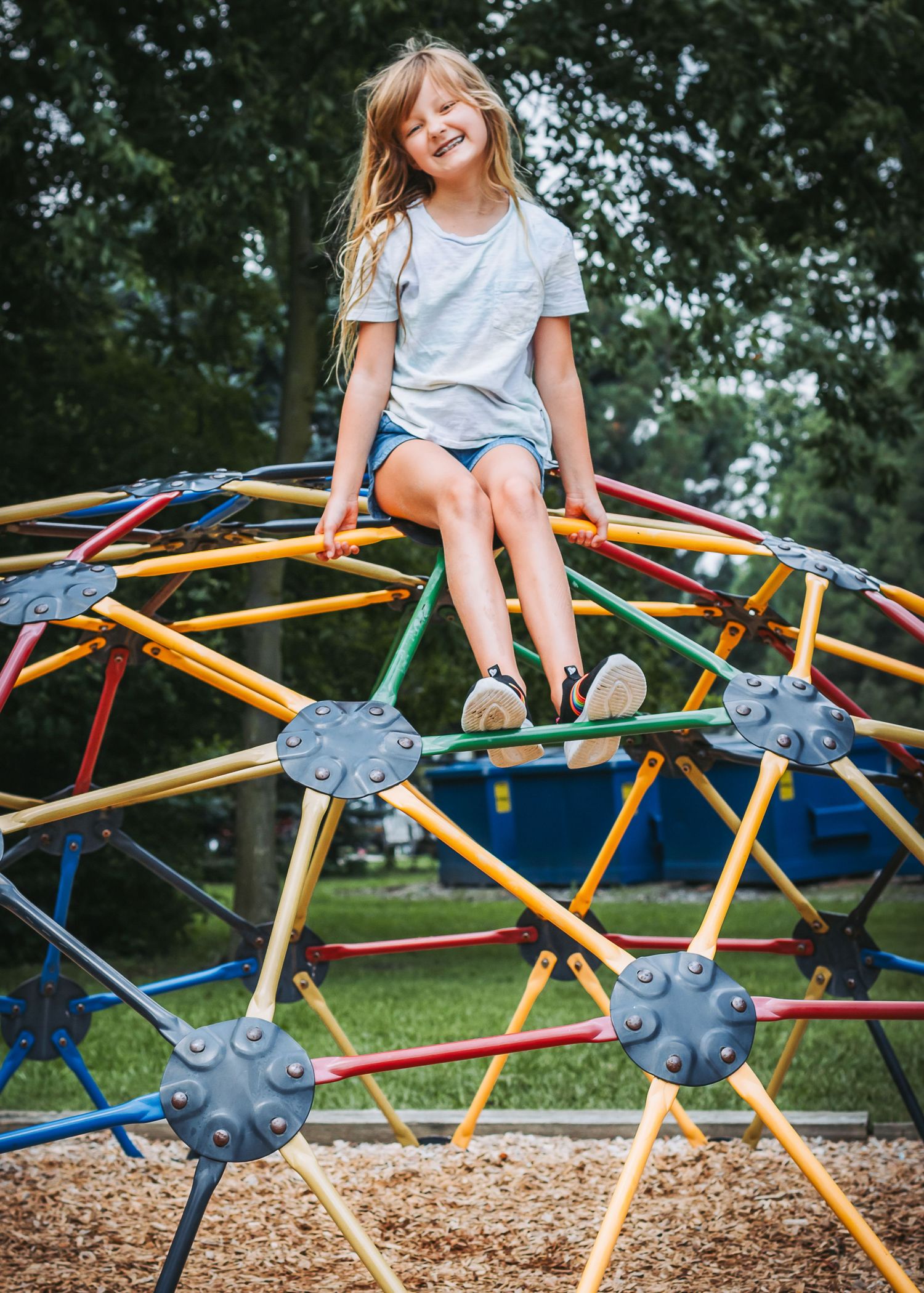 A child sits and plays on colorful geometric climbing equipment at an outdoor playground with mulch ground cover.