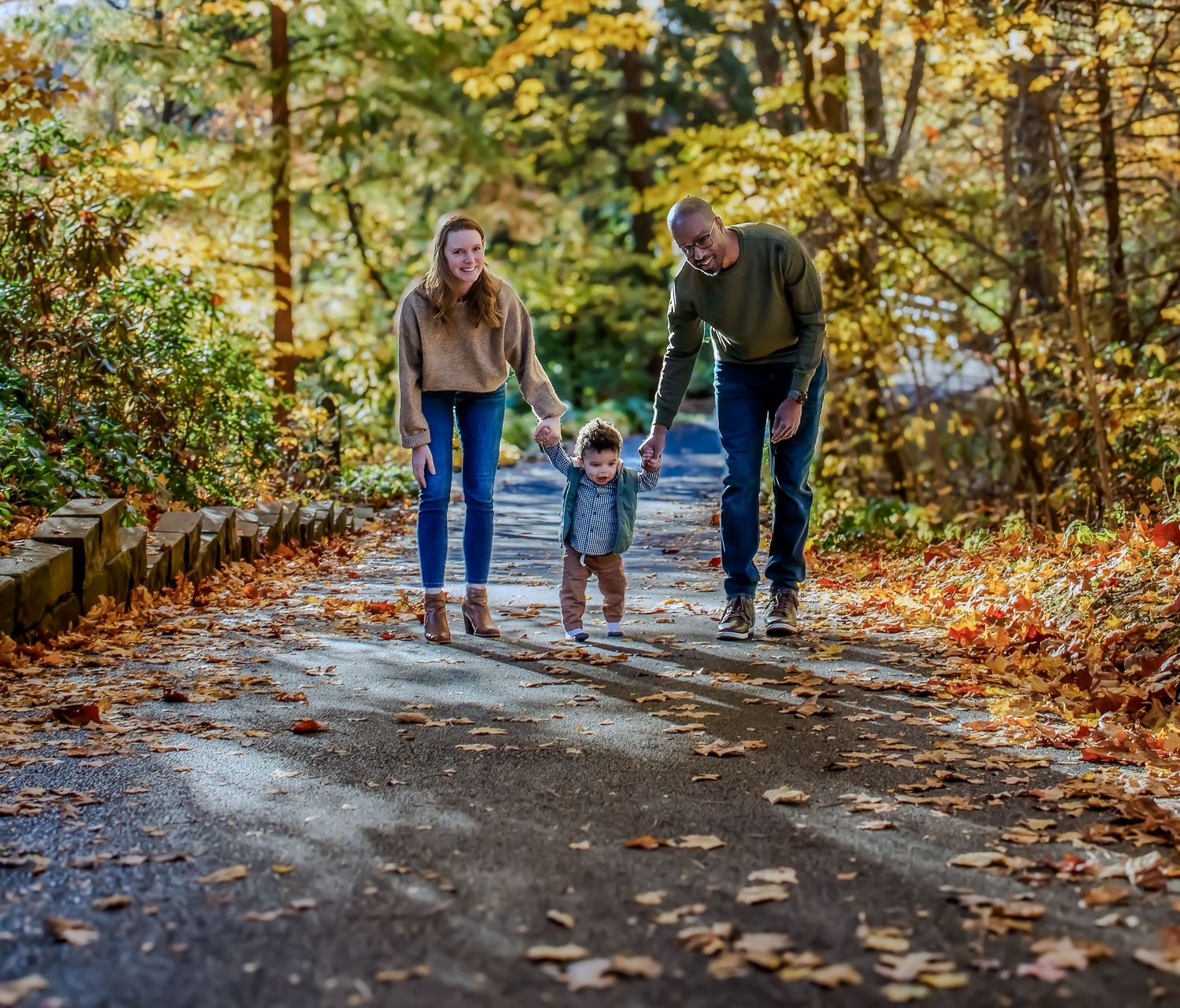 Three people walking together on a leaf-covered autumn forest path during a fall day.