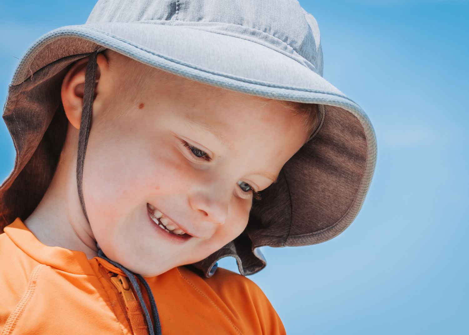 Smiling kid wearing protective sun hat against vibrant blue sky background.