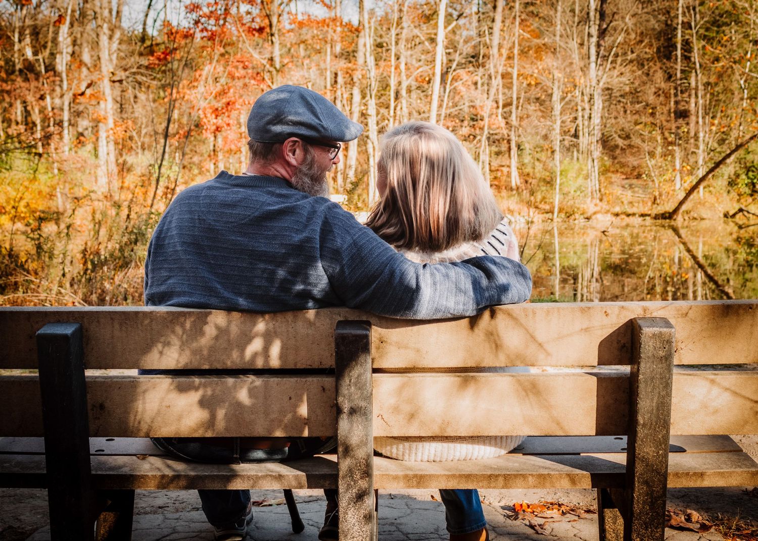 An intimate fall photoshoot on a wooden dock with trees showing autumn colors in the background.
