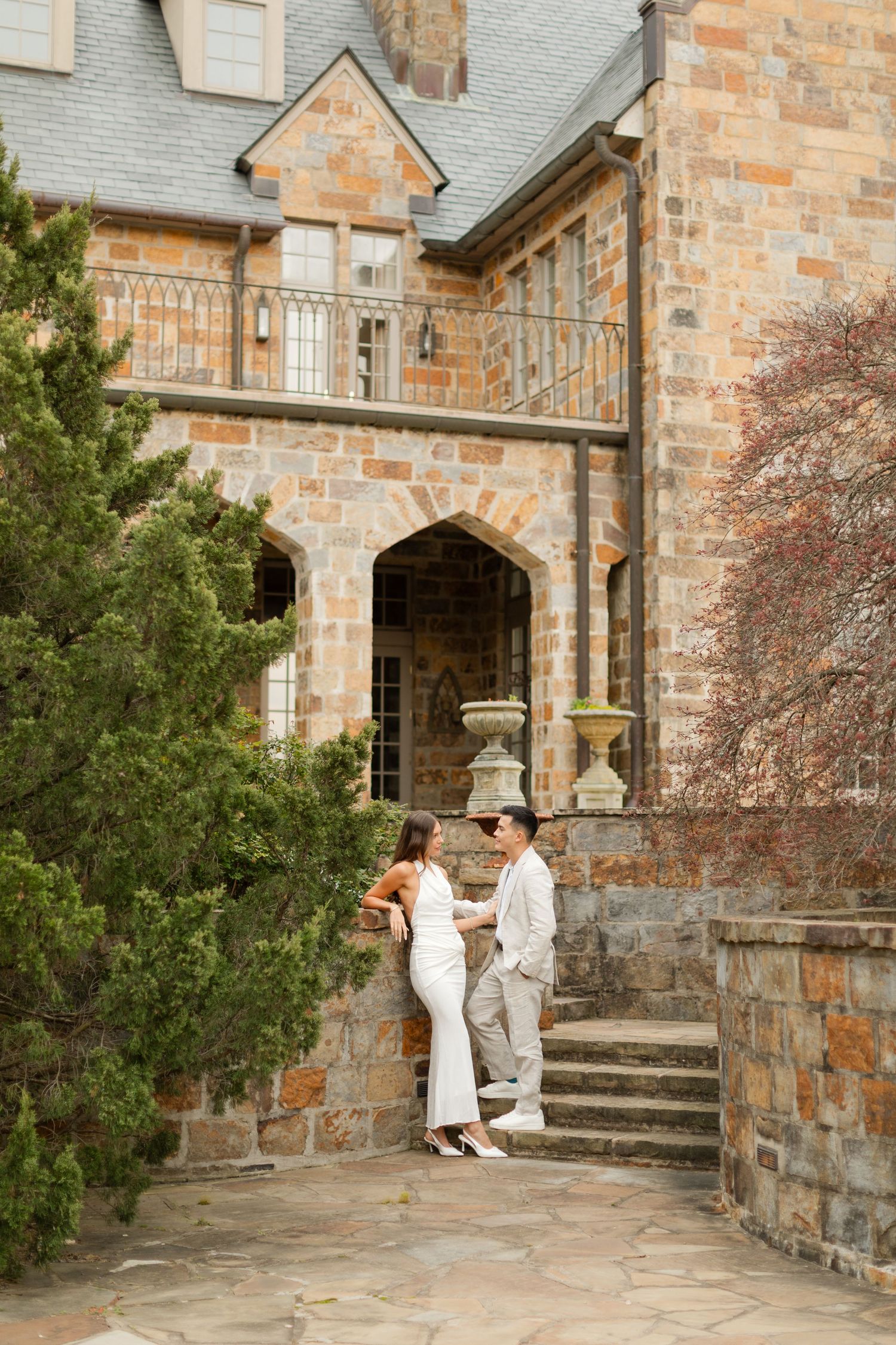 A couple shares an intimate moment on stone steps outside a historic stone church building. Goodwin Manor.