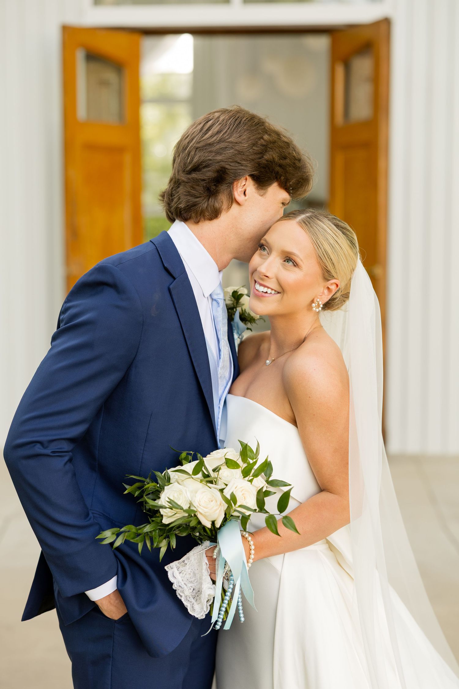 A wedding couple shares an intimate moment while the bride holds a white and green bouquet with blue accentsCold Springs Events
