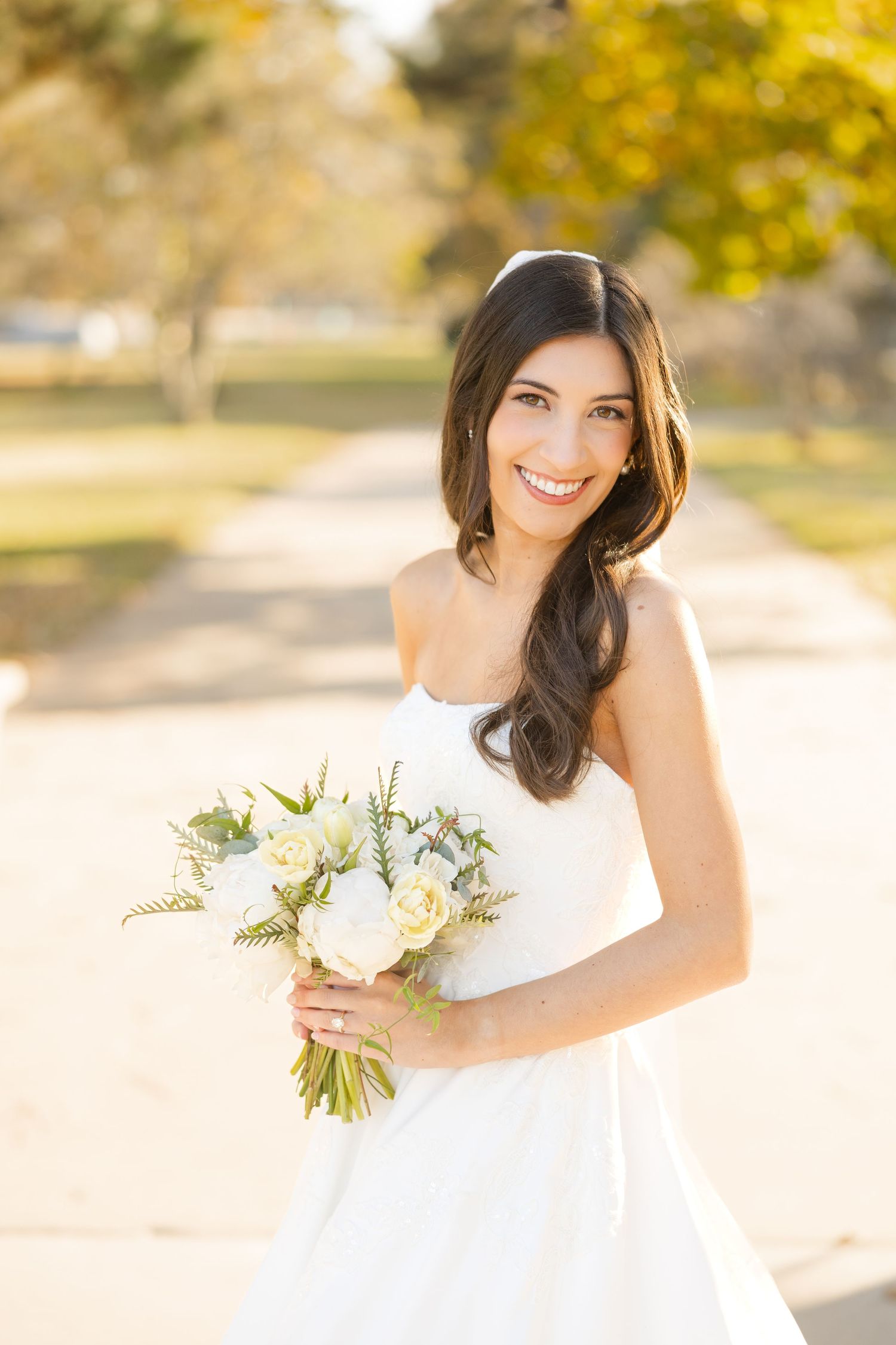 A white bridal bouquet with delicate flowers complements an elegant wedding dress in golden sunlight.
