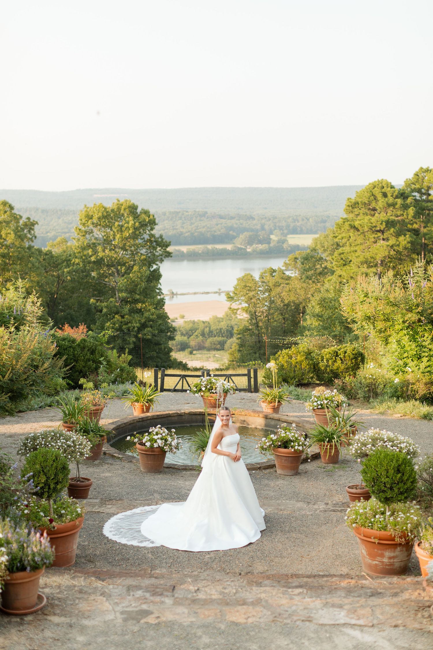 A scenic overlook with terracotta potted plants and a stone patio offers stunning views of a lake and rolling hills.