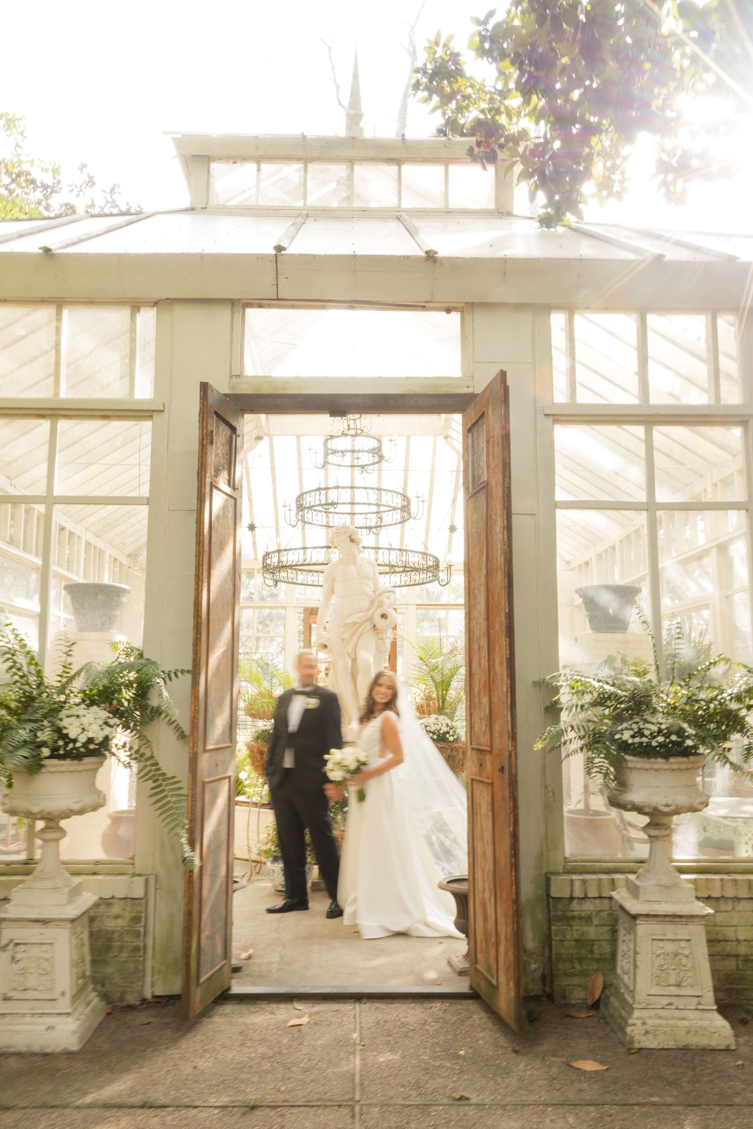 Couple stands in ornate greenhouse doorway during wedding ceremony.Marlgsate Plantation