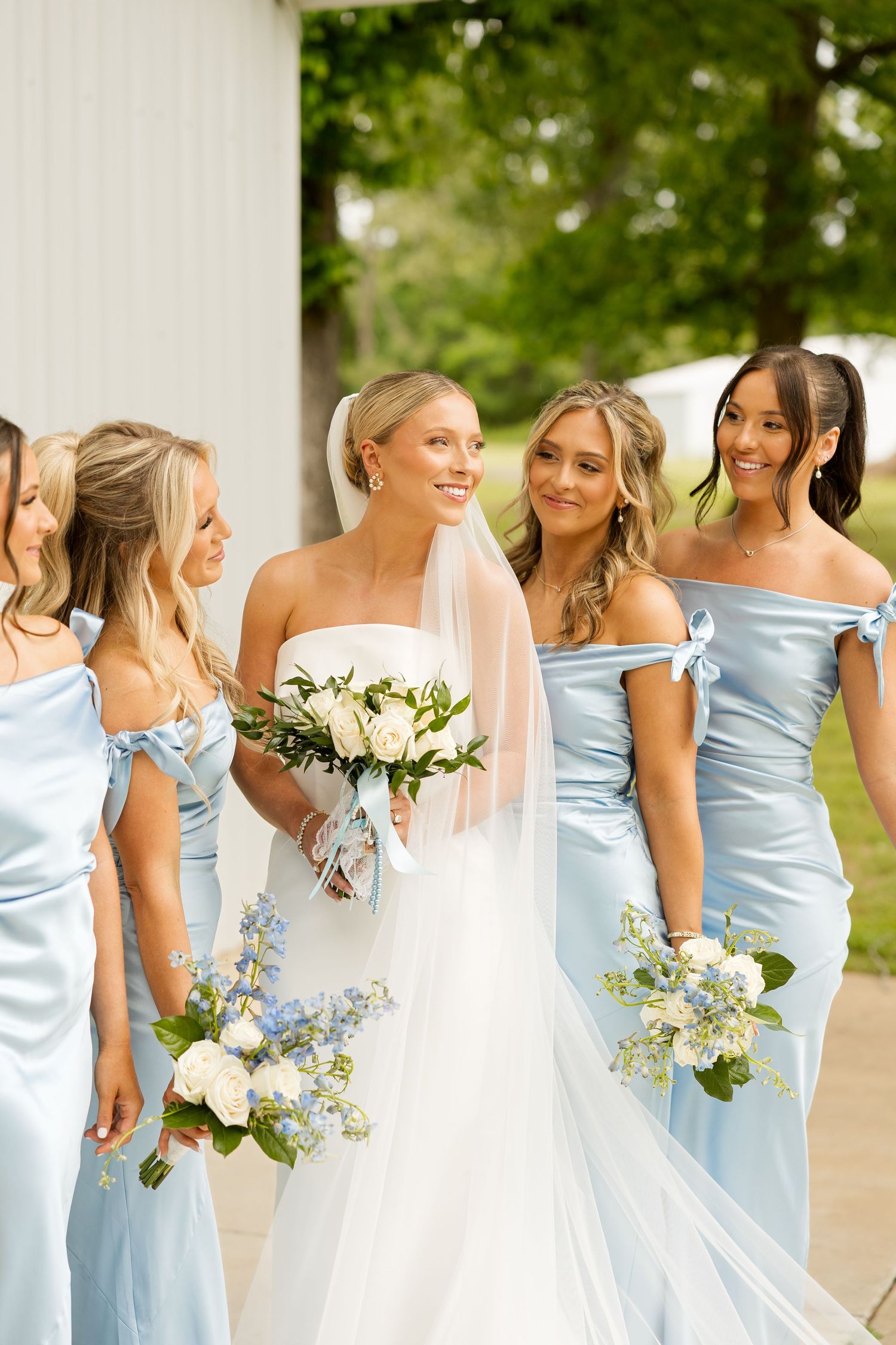 Bridesmaids in light blue satin dresses pose with bouquets of white and blue flowers.Cold Springs Events