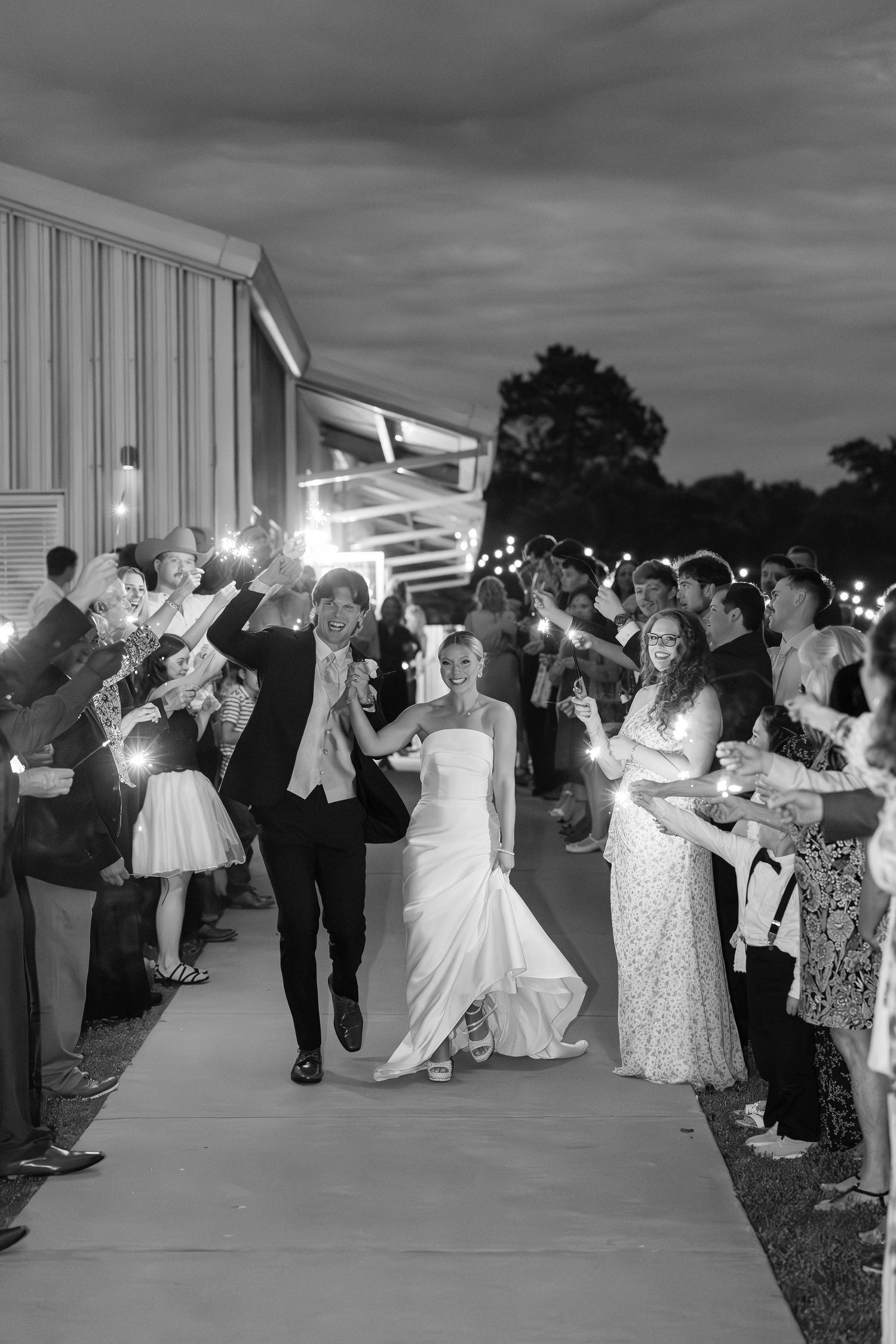 Wedding guests forming a sparkler exit tunnel at night outside a white venue.Cold Springs Events