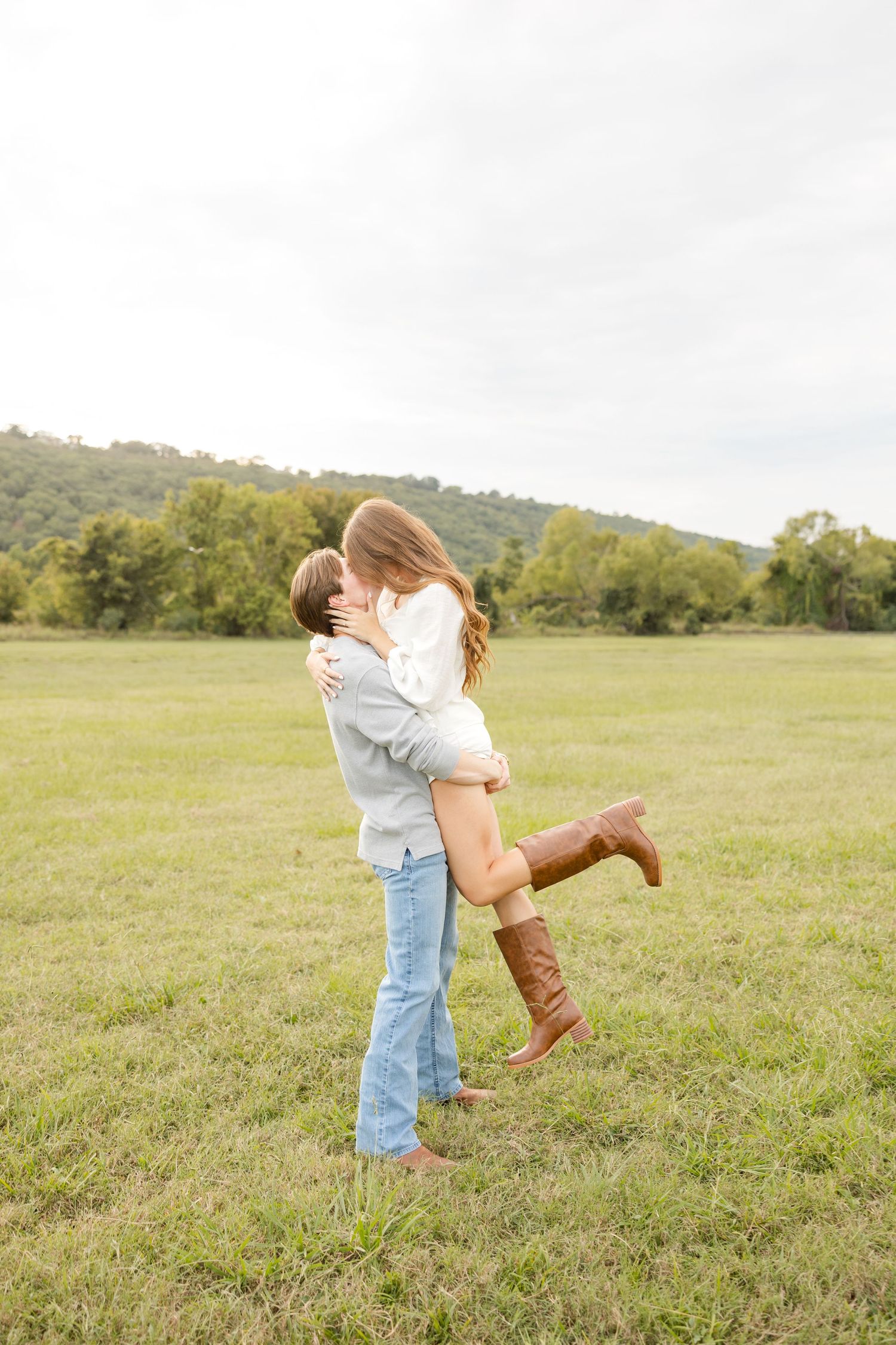 A romantic couple spins and embraces in a serene meadow with rolling hills in the background.