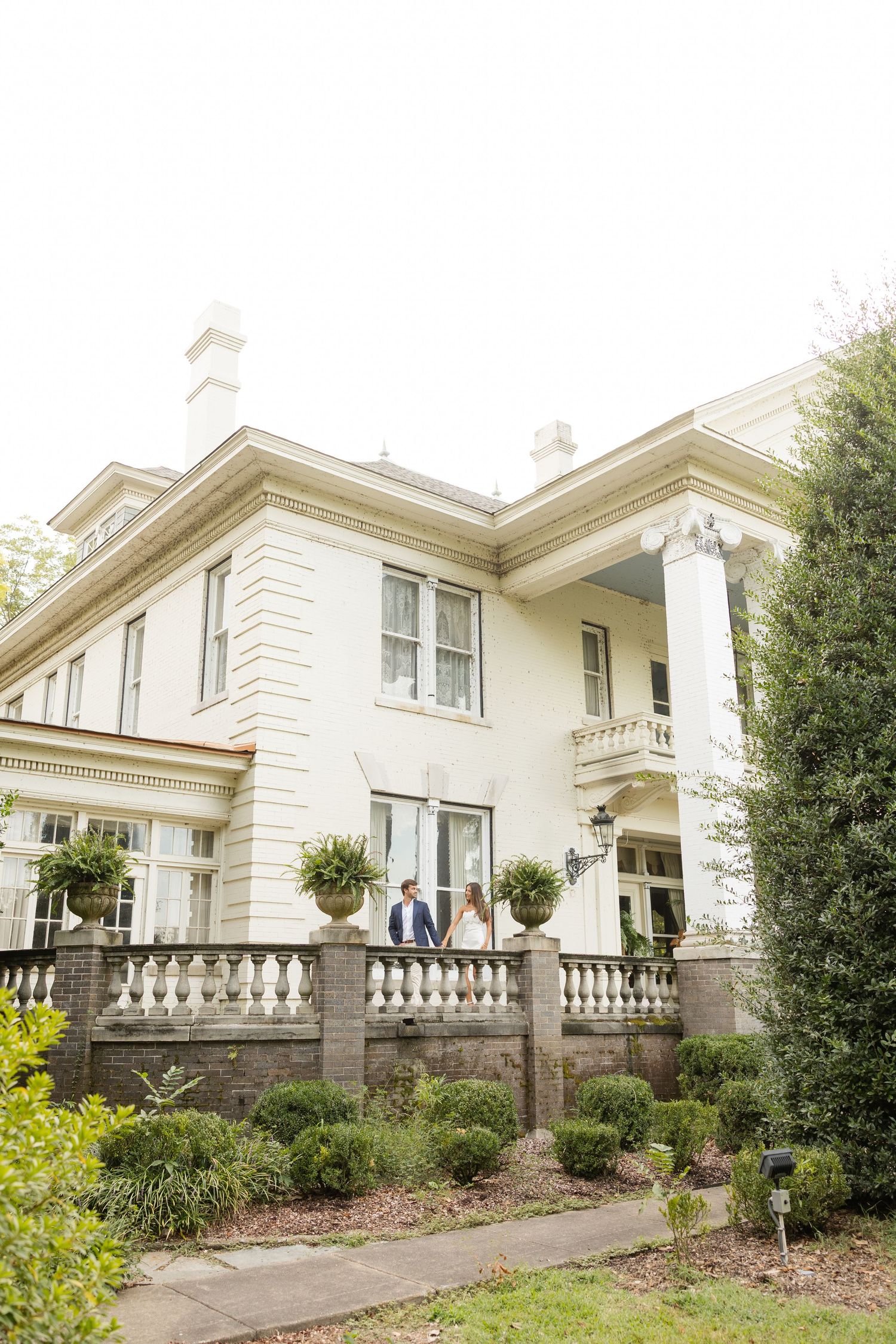 An elegant white mansion with classic columns and balustrades surrounded by manicured gardens.
