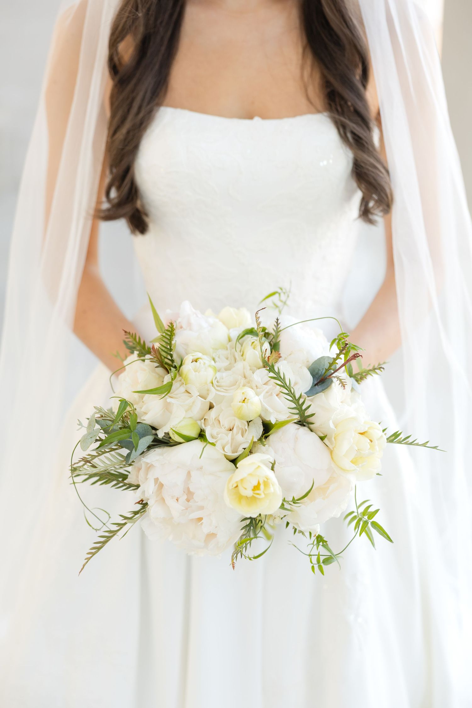 Close-up of white and cream bridal bouquet with roses and greenery against wedding dress.