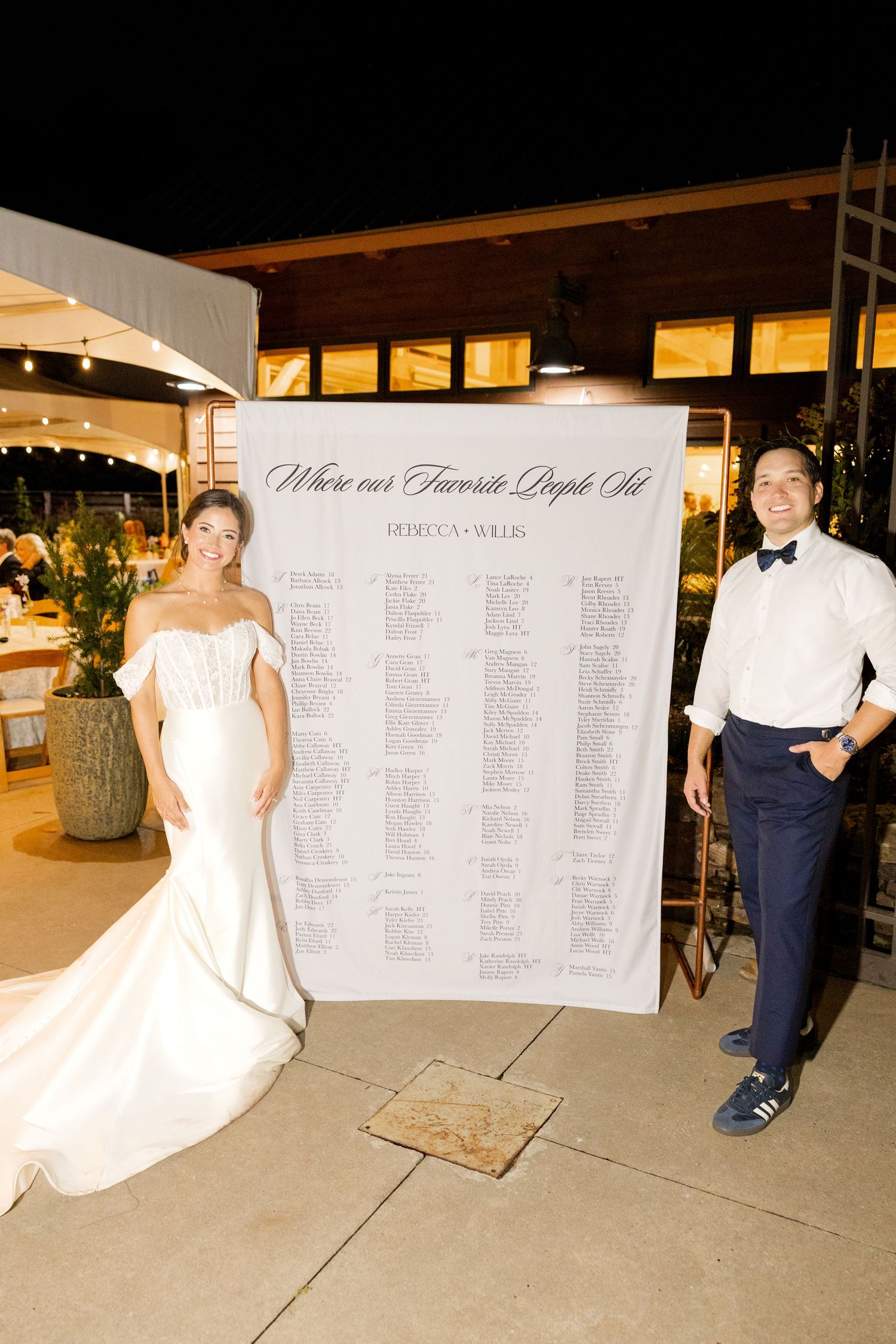 Wedding seating chart display with elegant white boards and text at an outdoor evening reception venue. Botanical Gardens of the Ozarks